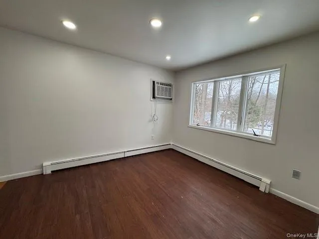 Empty room with dark wood-style flooring, baseboard heating, recessed lighting, and a wall unit AC Empty room with dark wood-style flooring, baseboard heating, recessed lighting, and a wall unit AC