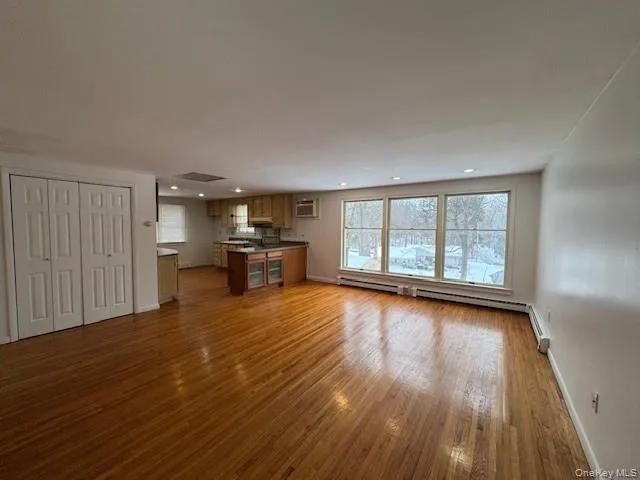 Unfurnished living room with dark wood-type flooring, recessed lighting, and a baseboard heating unit Unfurnished living room with dark wood-type flooring, recessed lighting, and a baseboard heating unit