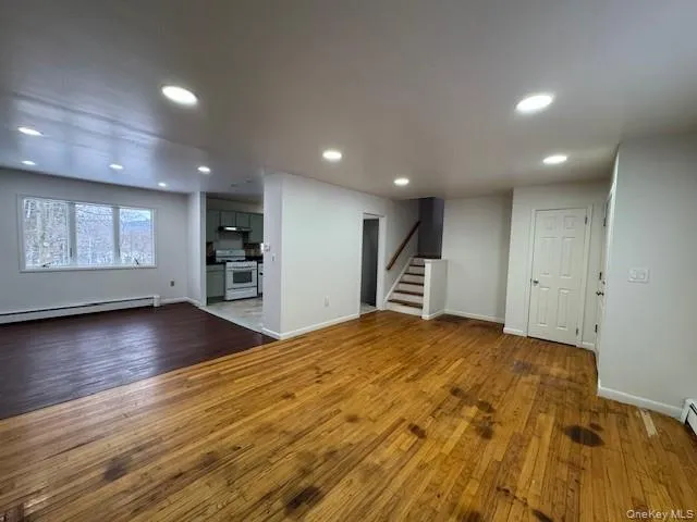 Unfurnished living room featuring dark wood-type flooring, stairway, a baseboard radiator, and recessed lighting Unfurnished living room featuring dark wood-type flooring, stairway, a baseboard radiator, and recessed lighting