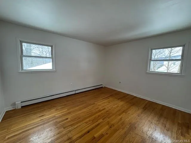 Empty room with baseboard heating, light wood finished floors, and healthy amount of natural light Empty room with baseboard heating, light wood finished floors, and healthy amount of natural light