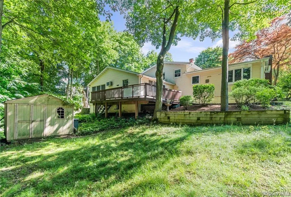 Back of house with a storage unit, a wooden deck, a lawn, and view of scattered trees Back of house with a storage unit, a wooden deck, a lawn, and view of scattered trees