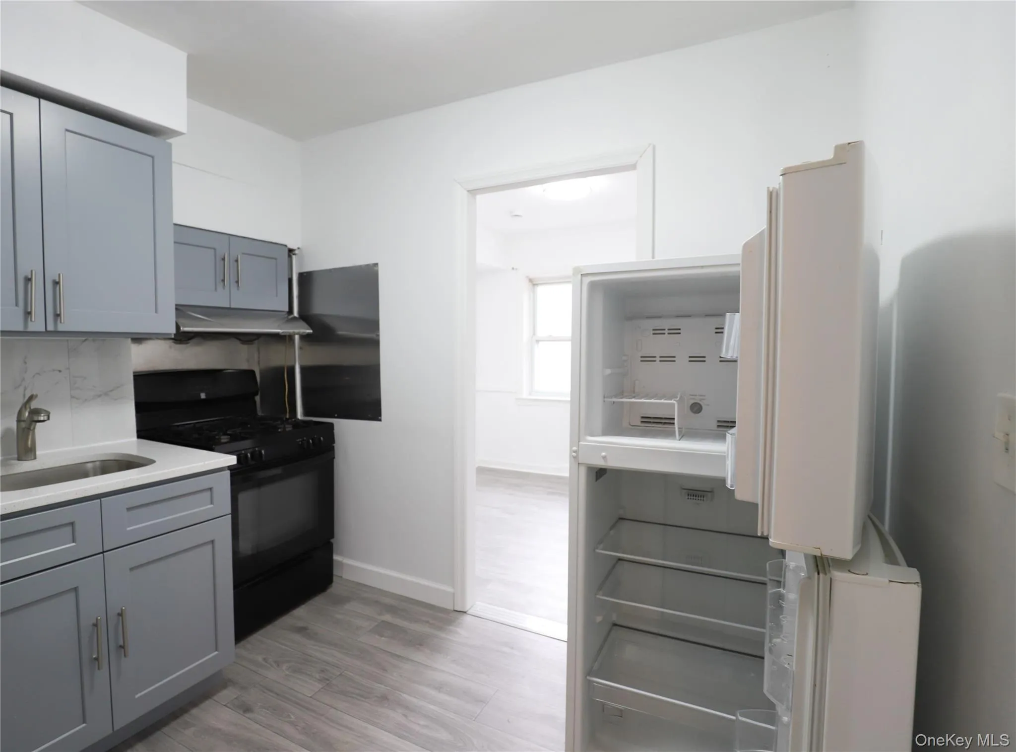 Kitchen with gray cabinetry, black gas range, light wood-style flooring, tasteful backsplash, and light stone countertops Kitchen with gray cabinetry, black gas range, light wood-style flooring, tasteful backsplash, and light stone countertops