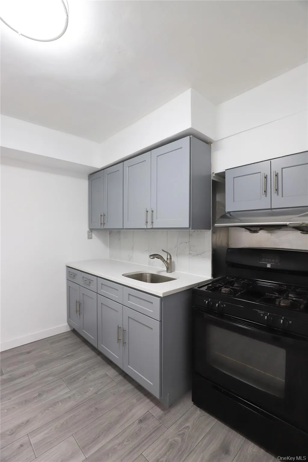 Kitchen featuring black range with gas stovetop, gray cabinets, light wood finished floors, and decorative backsplash Kitchen featuring black range with gas stovetop, gray cabinets, light wood finished floors, and decorative backsplash