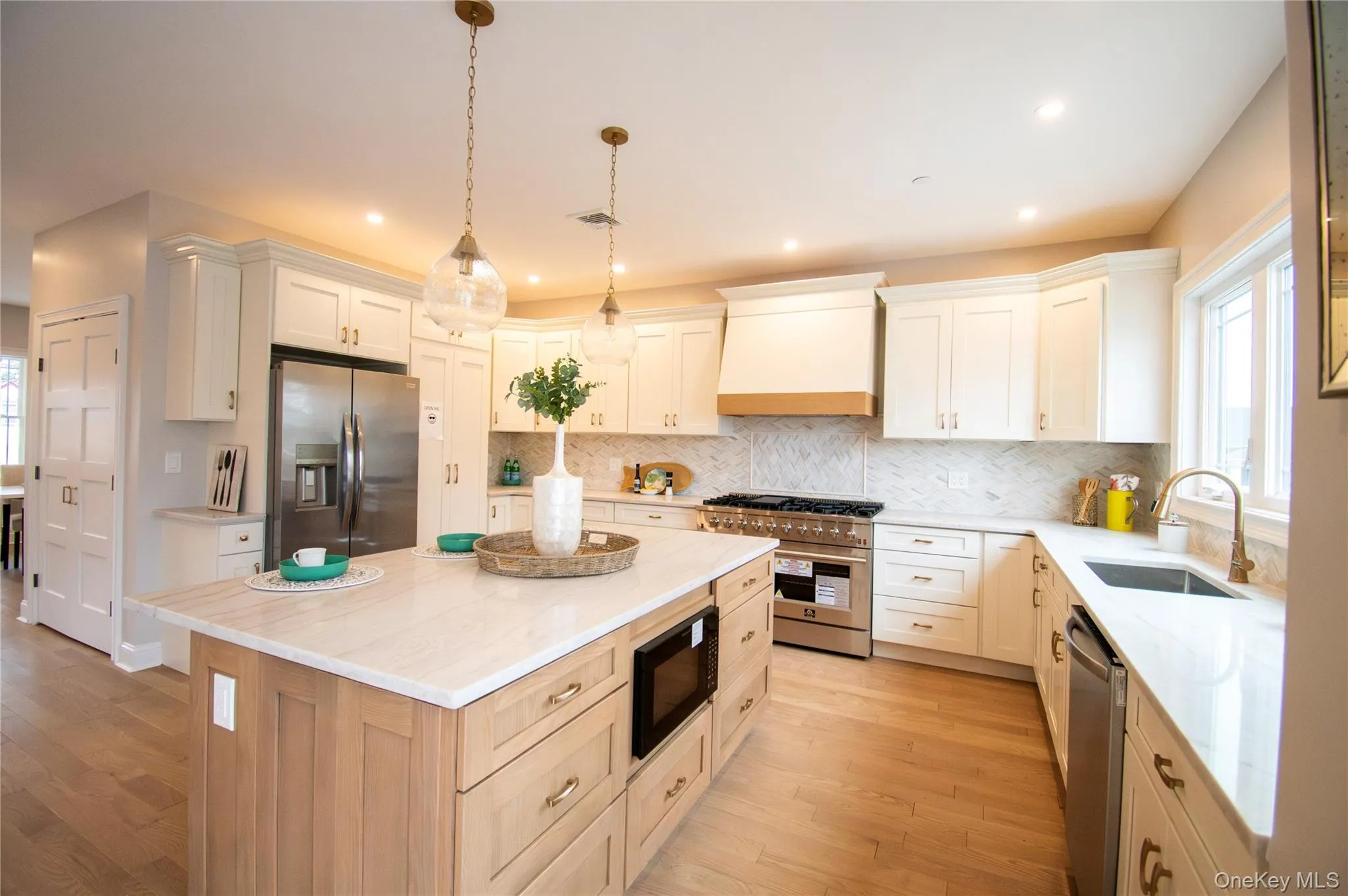 Kitchen with stainless steel appliances, decorative light fixtures, tasteful backsplash, light wood-type flooring, and light stone countertops Kitchen with stainless steel appliances, decorative light fixtures, tasteful backsplash, light wood-type flooring, and light stone countertops