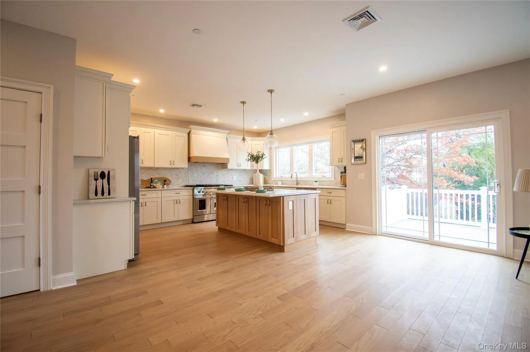 Kitchen featuring decorative light fixtures, backsplash, appliances with stainless steel finishes, light wood finished floors, and a center island Kitchen featuring decorative light fixtures, backsplash, appliances with stainless steel finishes, light wood finished floors, and a center island