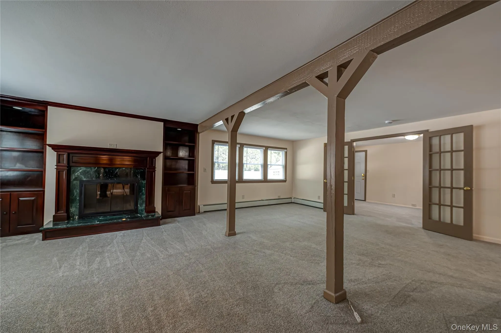 Spacious living area featuring a built-in fireplace with a stone surround, integrated shelving and cabinetry, soft gray carpeting, and multiple windows allowing natural light Spacious living area featuring a built-in fireplace with a stone surround, integrated shelving and cabinetry, soft gray carpeting, and multiple windows allowing natural light