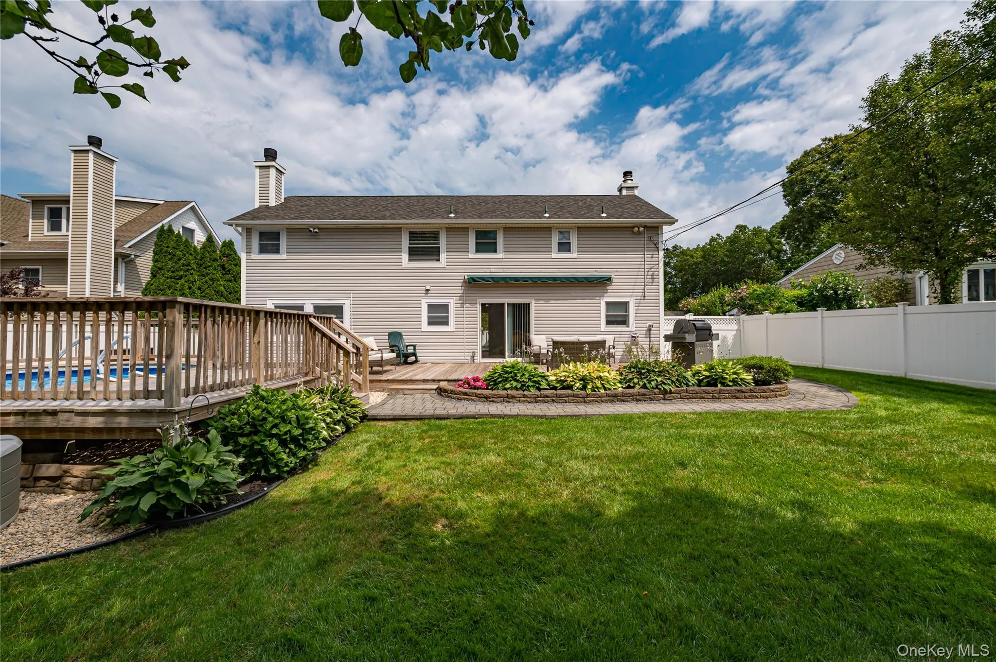 Expansive backyard featuring a large green lawn, a wooden deck with a built-in pool, and a paver patio Expansive backyard featuring a large green lawn, a wooden deck with a built-in pool, and a paver patio