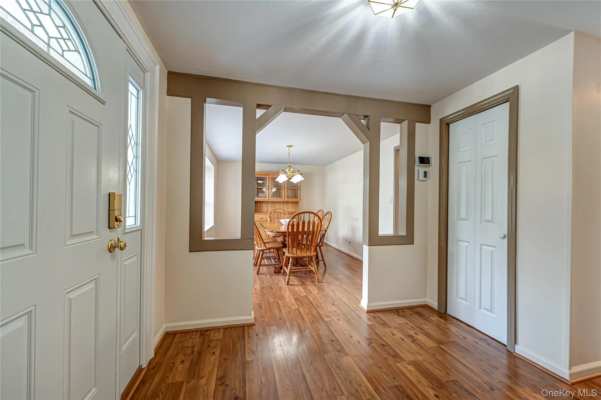 Entryway featuring wood-finish flooring, a white paneled door with decorative glass, and brass hardware Entryway featuring wood-finish flooring, a white paneled door with decorative glass, and brass hardware