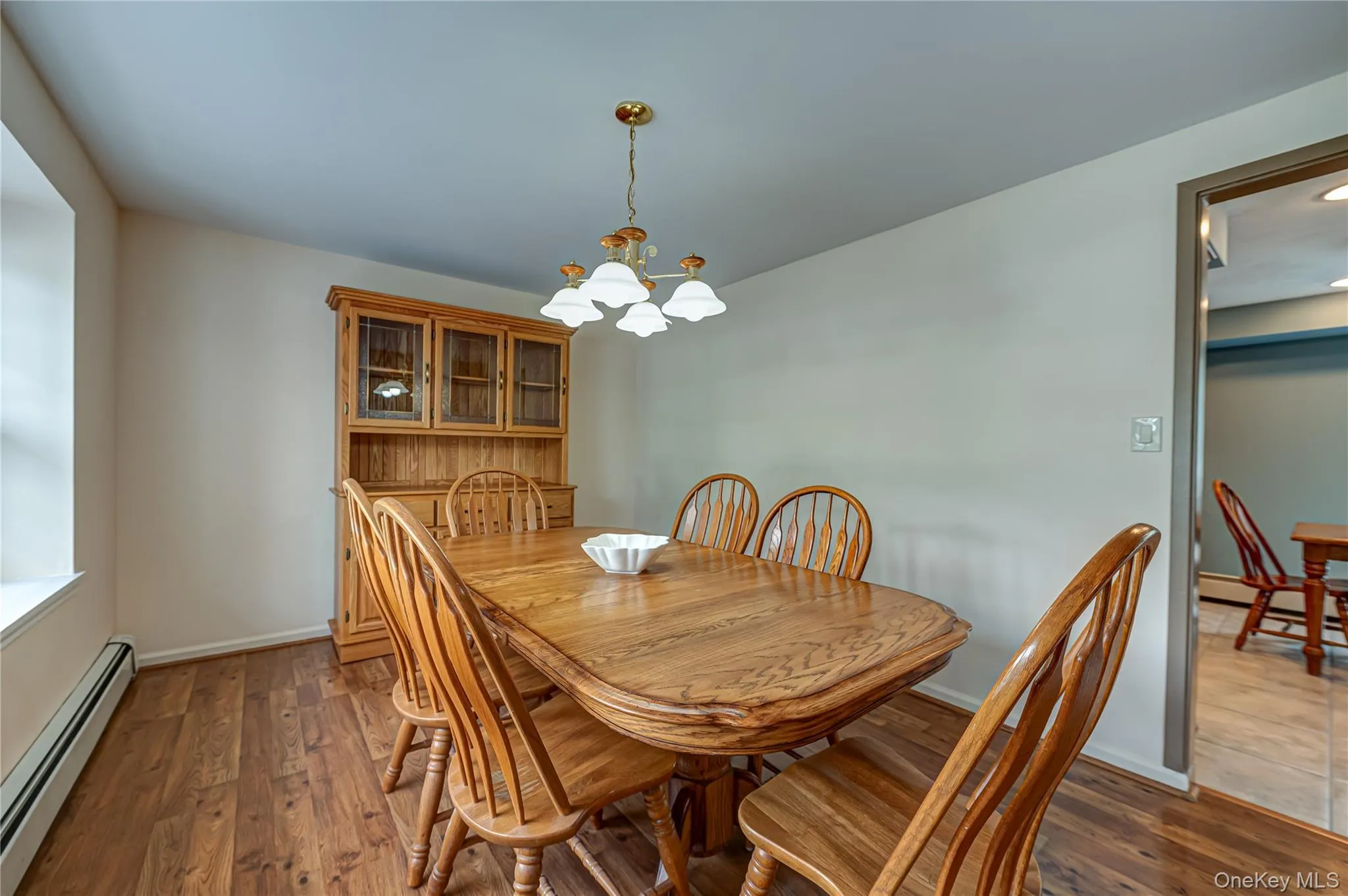 Spacious dining area featuring wood-finish flooring, a window, and a light fixture with frosted glass shades Spacious dining area featuring wood-finish flooring, a window, and a light fixture with frosted glass shades