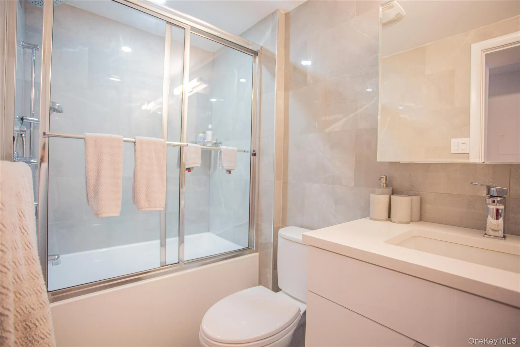 Bathroom with tile walls, vanity, bath / shower combo with glass door, and decorative backsplash Bathroom with tile walls, vanity, bath / shower combo with glass door, and decorative backsplash