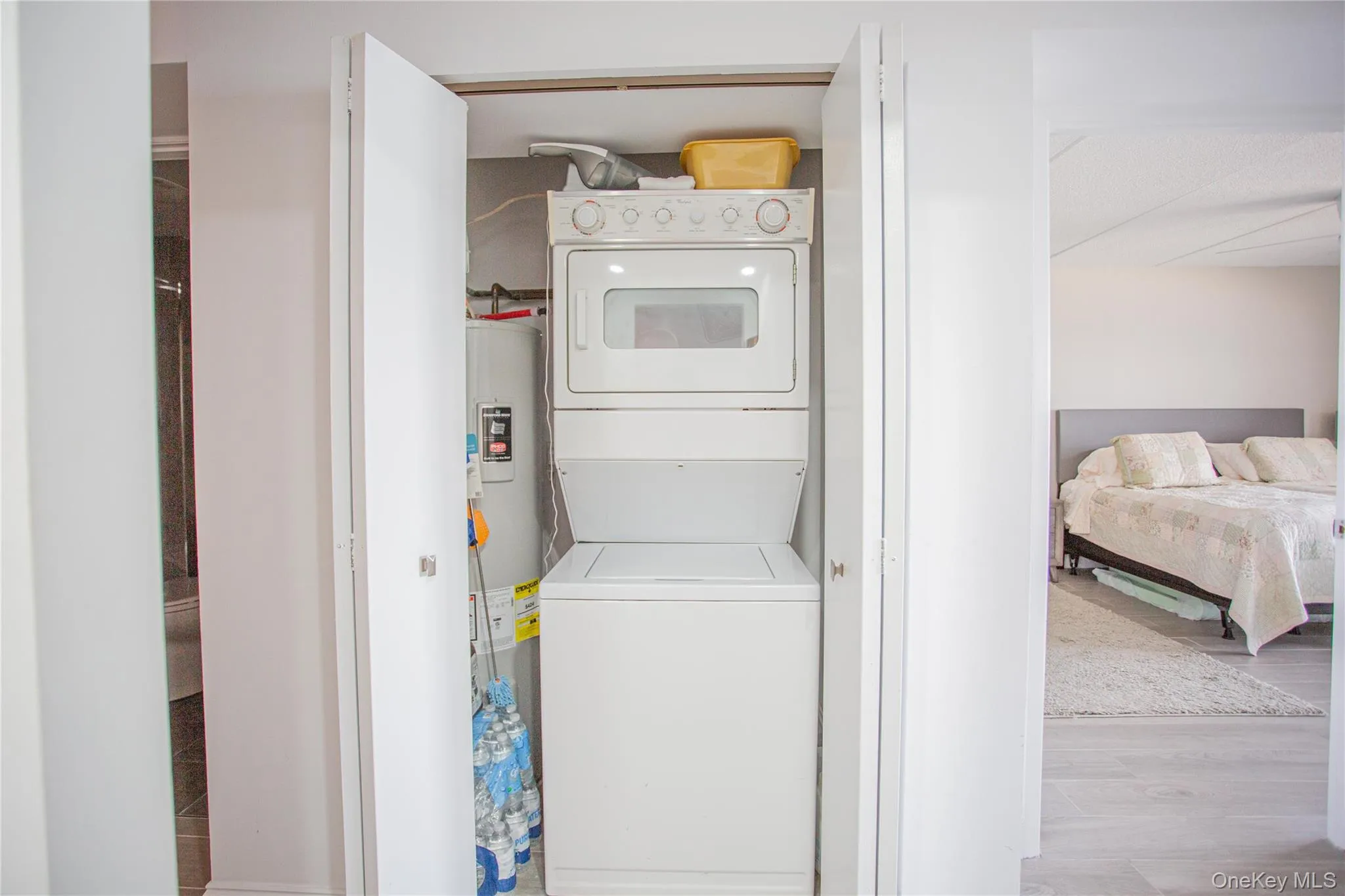 Laundry room featuring stacked washing machine and dryer, wood finished floors, and water heater Laundry room featuring stacked washing machine and dryer, wood finished floors, and water heater