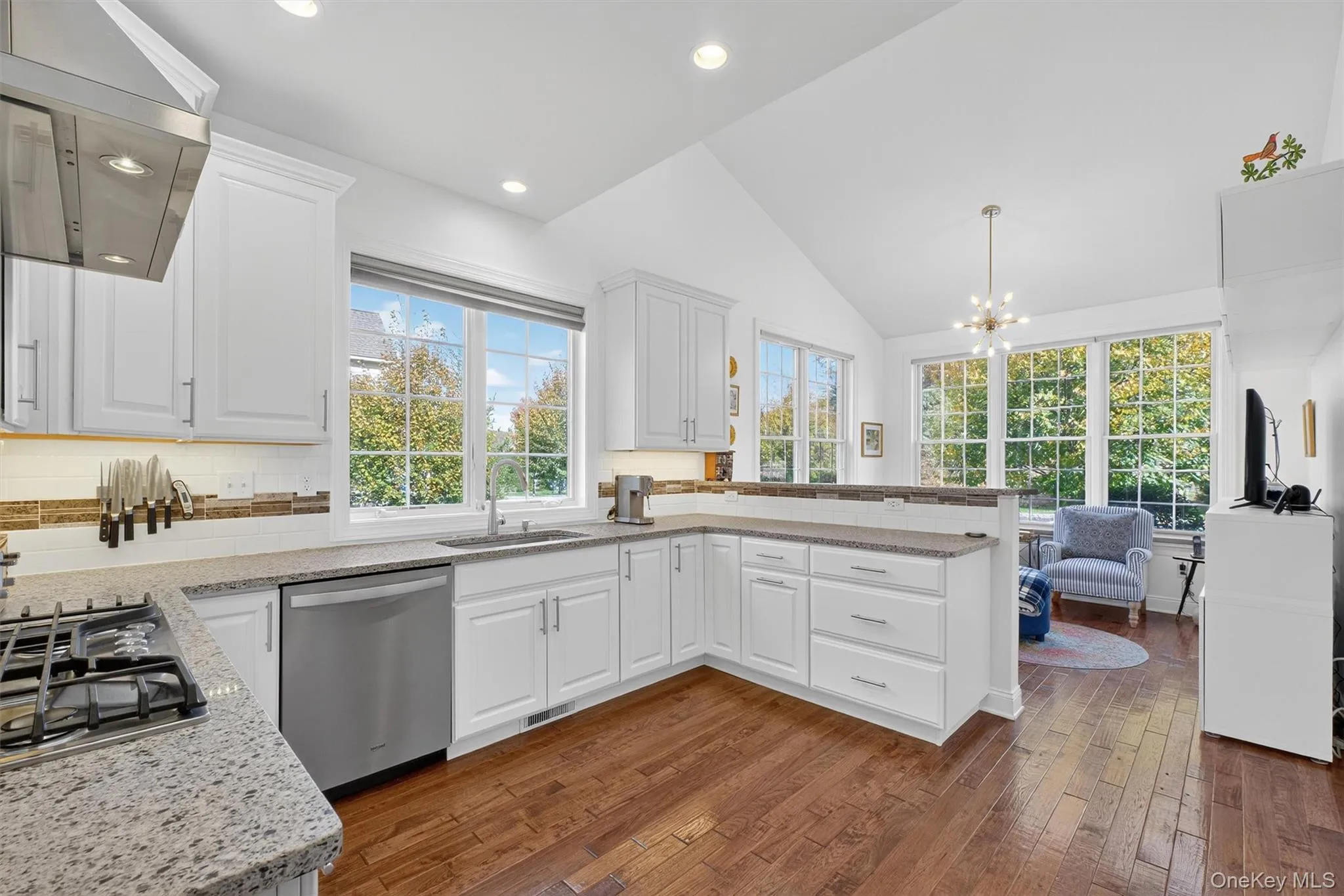 Kitchen with wall chimney exhaust hood, white cabinets, backsplash, dark wood finished floors, and lofted ceiling Kitchen with wall chimney exhaust hood, white cabinets, backsplash, dark wood finished floors, and lofted ceiling