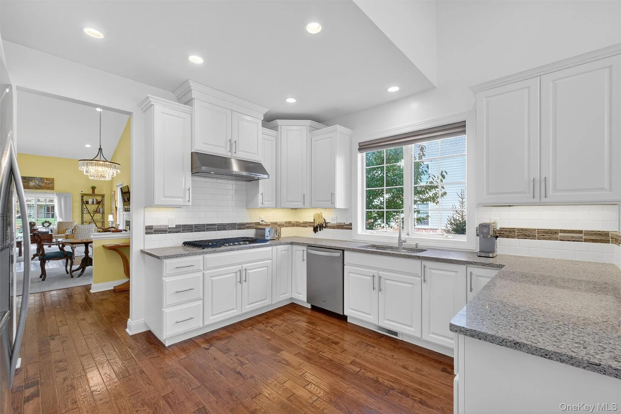 Kitchen with white cabinets, dark wood finished floors, light stone countertops, tasteful backsplash, and recessed lighting Kitchen with white cabinets, dark wood finished floors, light stone countertops, tasteful backsplash, and recessed lighting