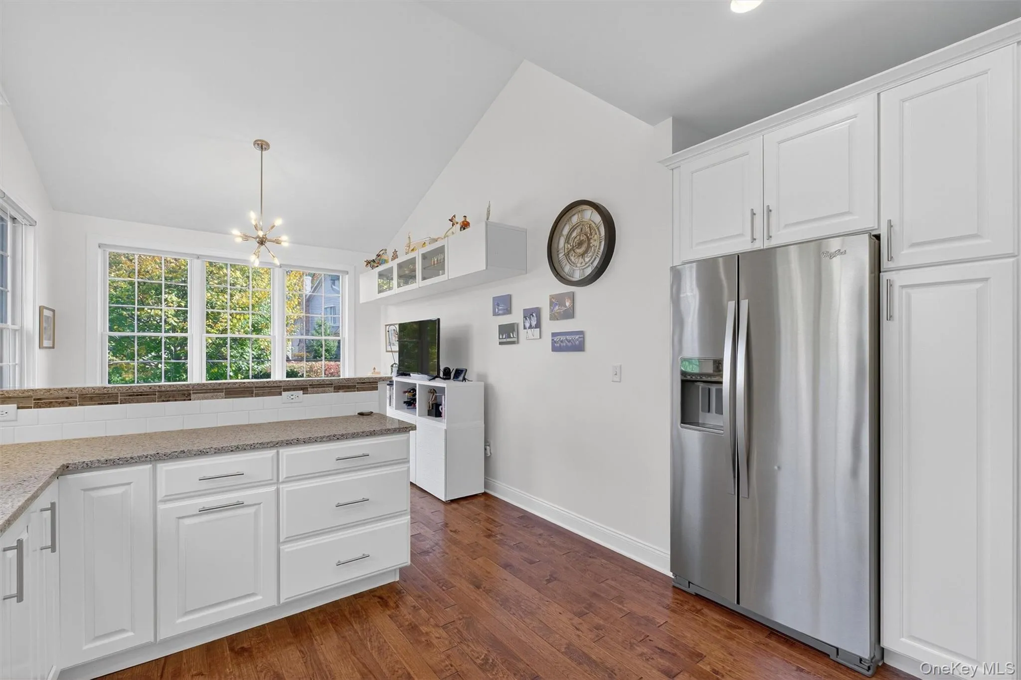 Kitchen featuring white cabinets, stainless steel refrigerator with ice dispenser, lofted ceiling, dark wood-type flooring, and light stone counters Kitchen featuring white cabinets, stainless steel refrigerator with ice dispenser, lofted ceiling, dark wood-type flooring, and light stone counters