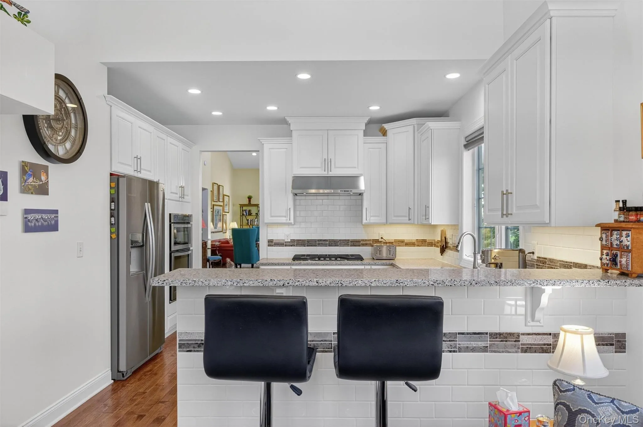 Kitchen with white cabinets, a peninsula, dark wood-style flooring, appliances with stainless steel finishes, and a kitchen breakfast bar Kitchen with white cabinets, a peninsula, dark wood-style flooring, appliances with stainless steel finishes, and a kitchen breakfast bar