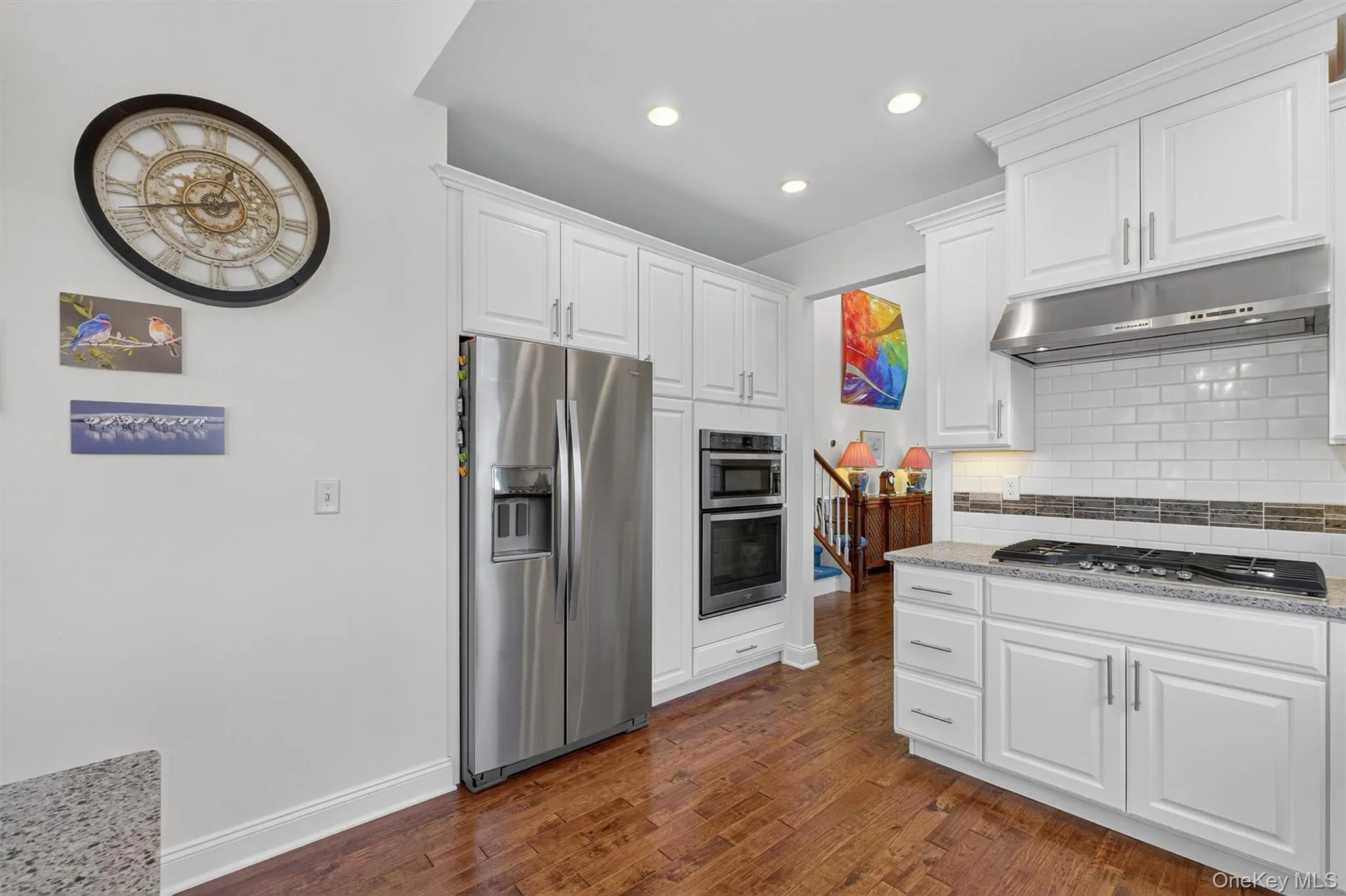 Kitchen featuring backsplash, stainless steel appliances, white cabinets, under cabinet range hood, and dark wood finished floors Kitchen featuring backsplash, stainless steel appliances, white cabinets, under cabinet range hood, and dark wood finished floors