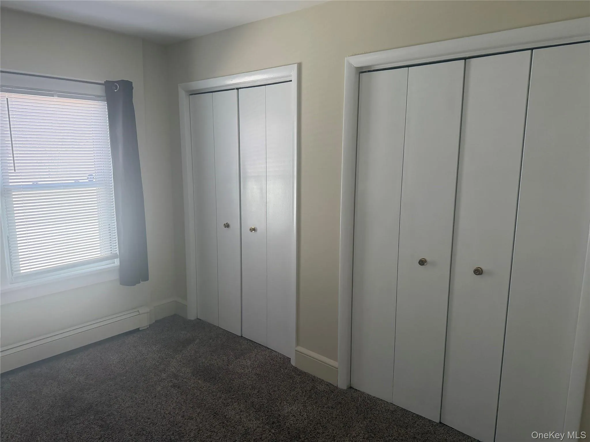 Primary bedroom with multiple closets, carpet floors, and baseboard heat. Primary bedroom with multiple closets, carpet floors, and baseboard heat.