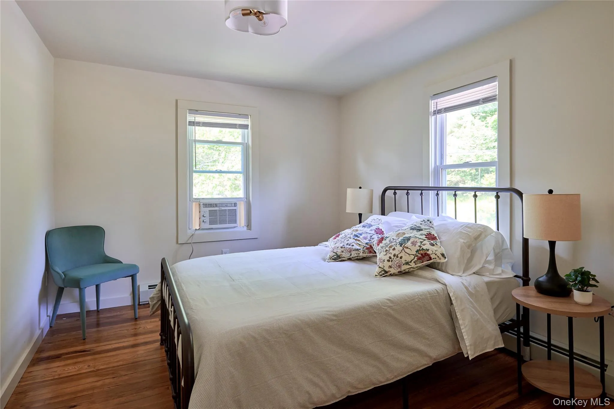 Bedroom with a baseboard radiator, multiple windows, dark wood-style floors, and cooling unit Bedroom with a baseboard radiator, multiple windows, dark wood-style floors, and cooling unit
