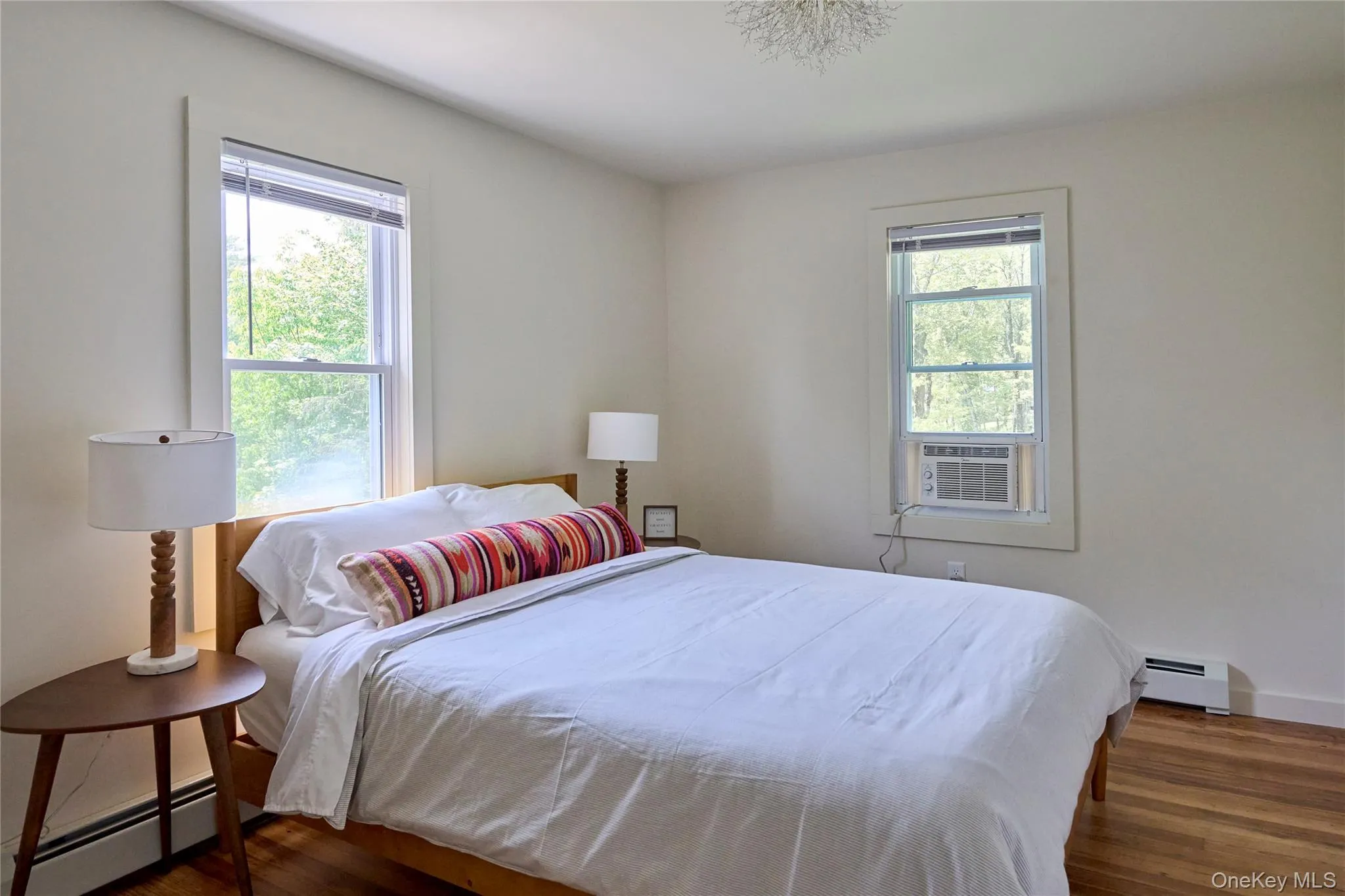 Bedroom with a baseboard heating unit, multiple windows, and wood finished floors Bedroom with a baseboard heating unit, multiple windows, and wood finished floors