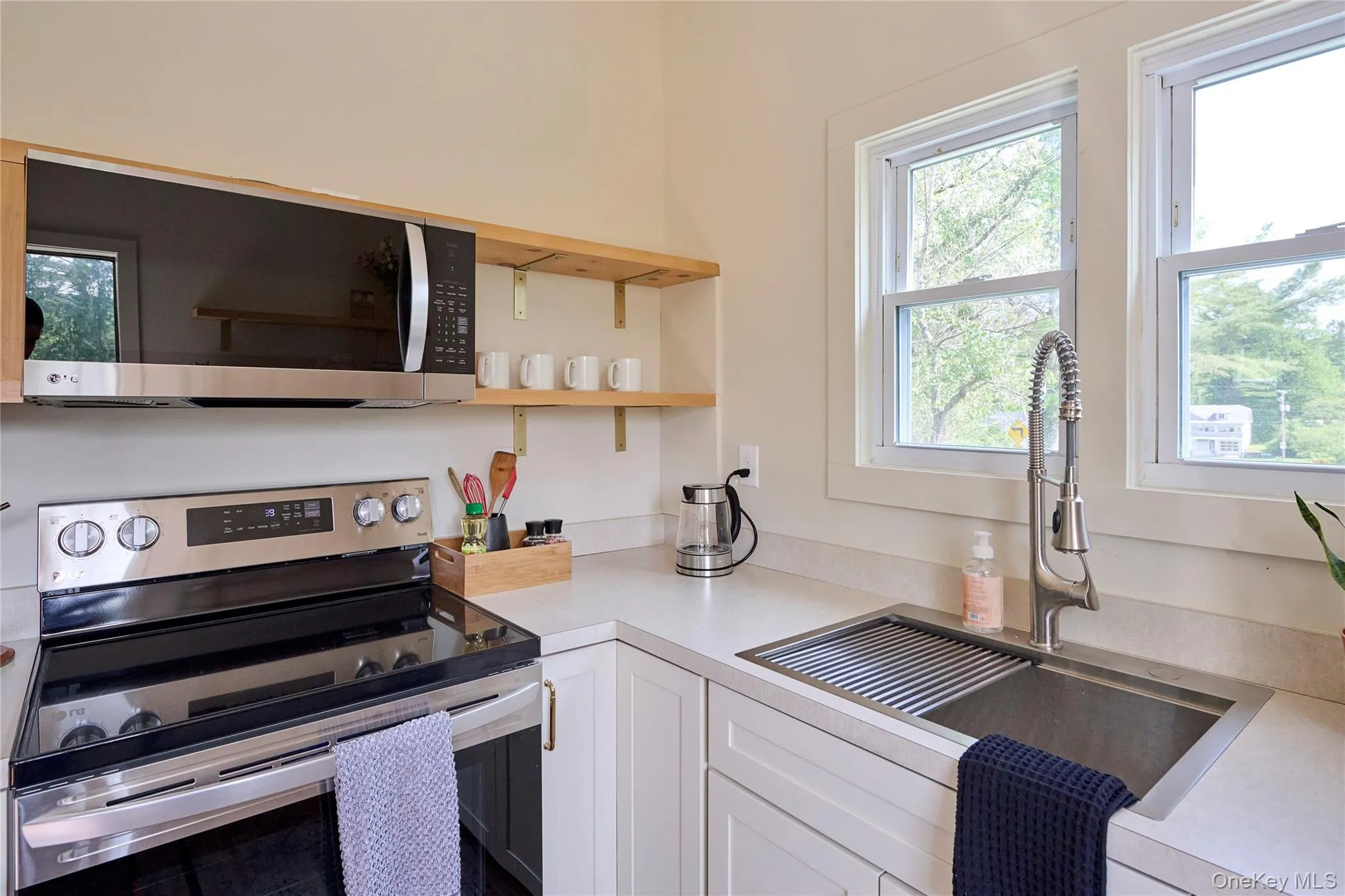 Kitchen featuring stainless steel appliances, a sink, white cabinets, light countertops, and open shelves Kitchen featuring stainless steel appliances, a sink, white cabinets, light countertops, and open shelves