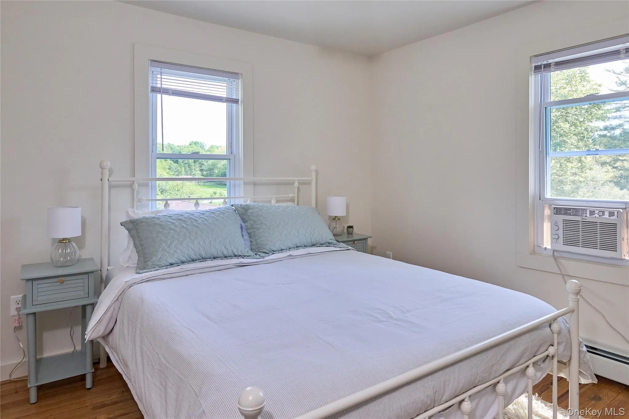 Bedroom featuring wood finished floors, a baseboard heating unit, and cooling unit Bedroom featuring wood finished floors, a baseboard heating unit, and cooling unit