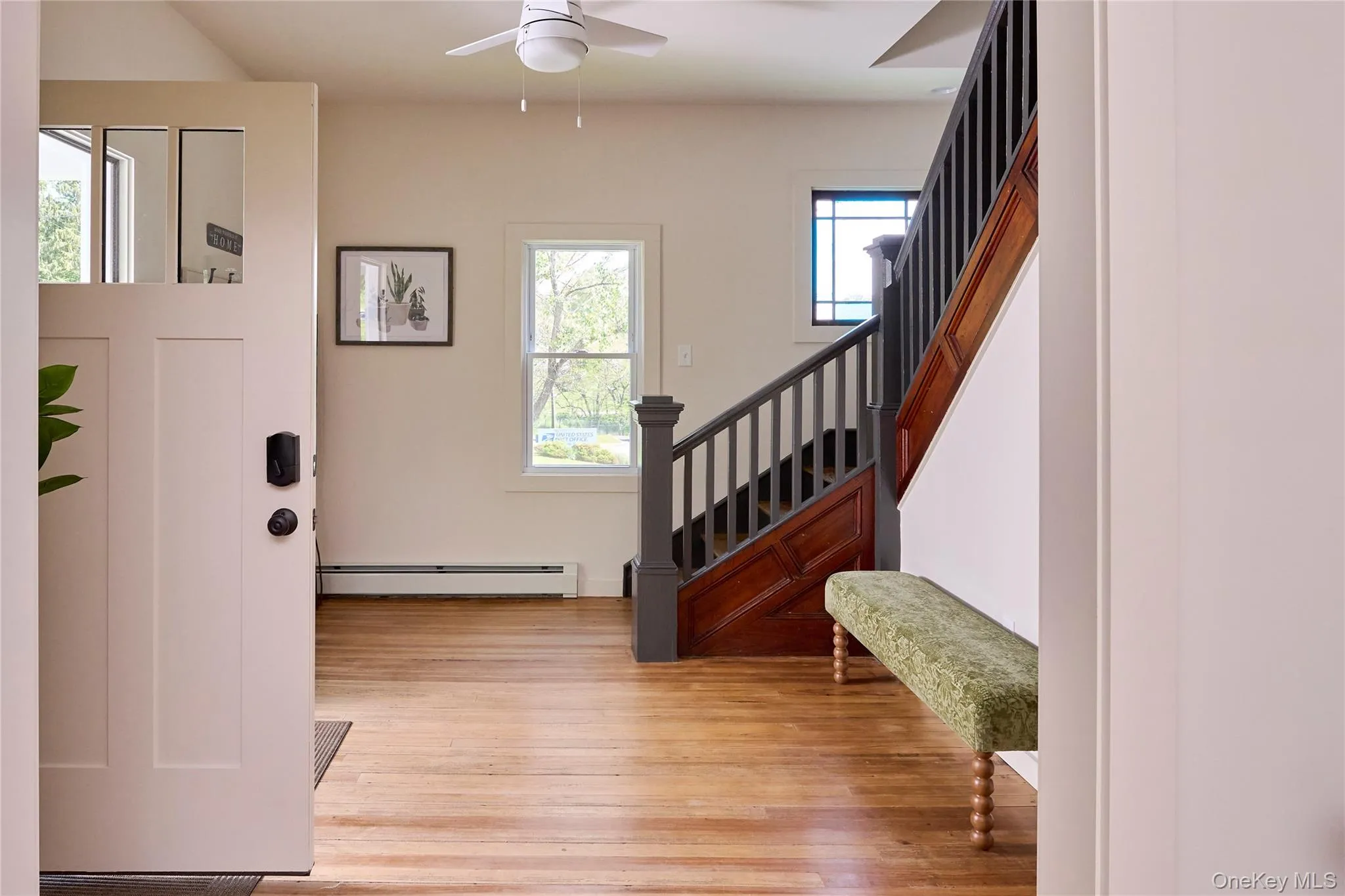 Foyer entrance with a baseboard heating unit, wood finished floors, a ceiling fan, and stairway Foyer entrance with a baseboard heating unit, wood finished floors, a ceiling fan, and stairway