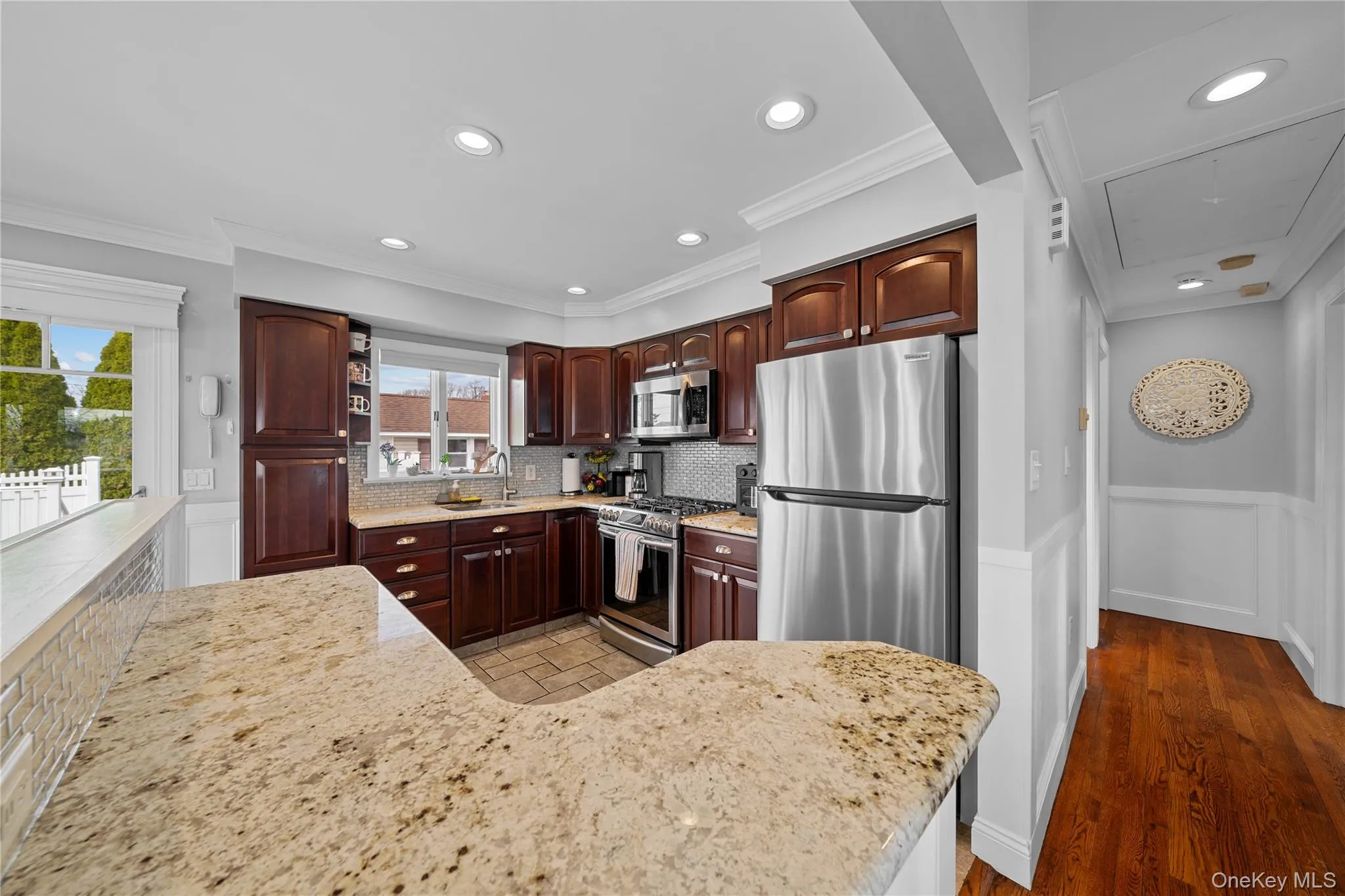 Kitchen featuring a wainscoted wall, stainless steel appliances, light stone counters, backsplash, and ornamental molding Kitchen featuring a wainscoted wall, stainless steel appliances, light stone counters, backsplash, and ornamental molding