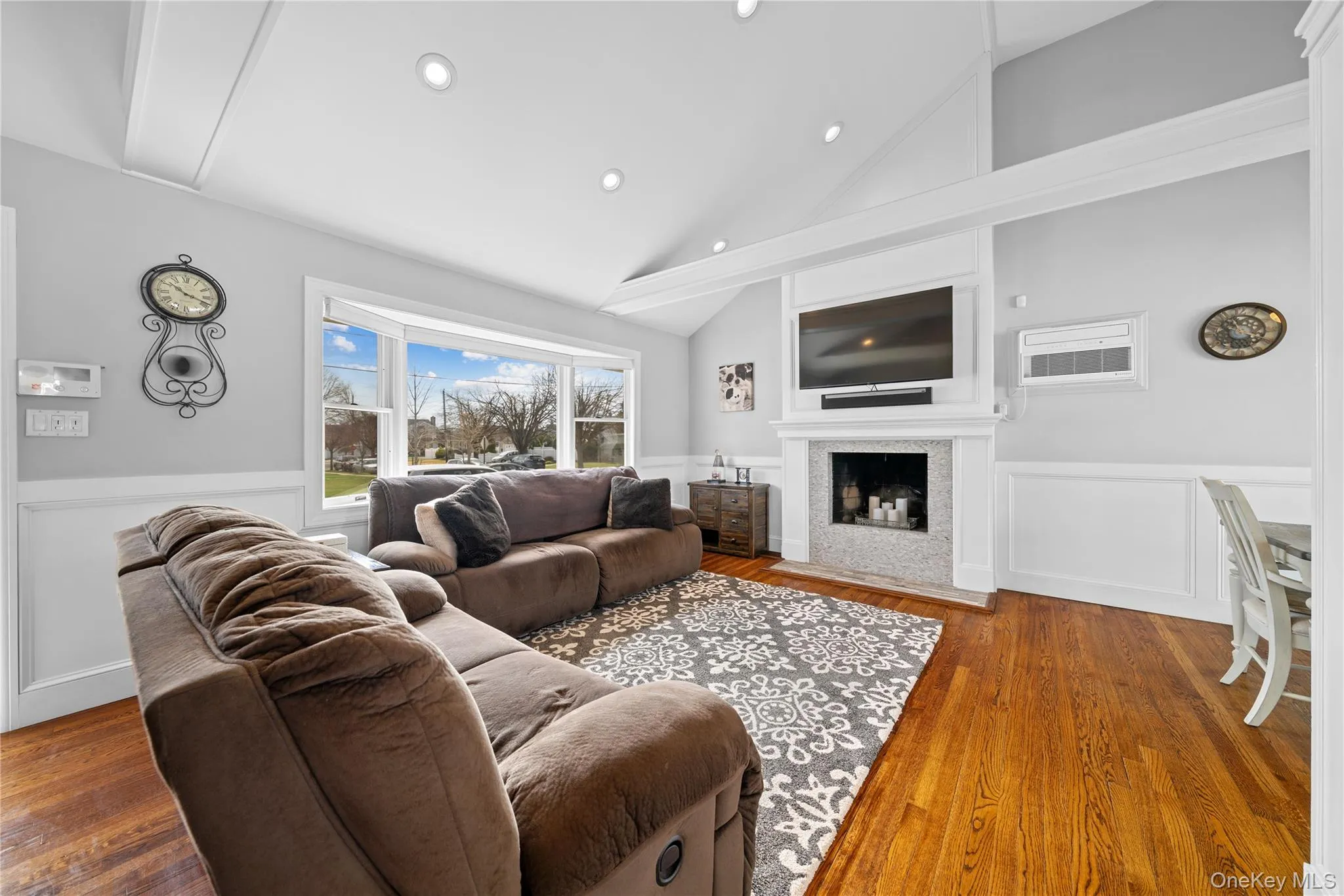 Living room with a wainscoted wall, a decorative wall, wood finished floors, lofted ceiling, and a fireplace with flush hearth Living room with a wainscoted wall, a decorative wall, wood finished floors, lofted ceiling, and a fireplace with flush hearth