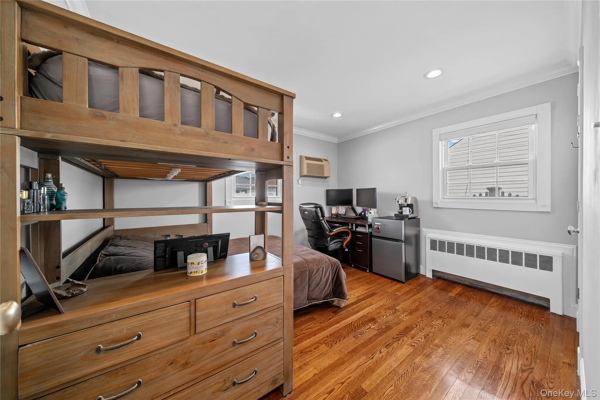 Bedroom with crown molding, radiator, an office area, freestanding refrigerator, and dark wood finished floors Bedroom with crown molding, radiator, an office area, freestanding refrigerator, and dark wood finished floors