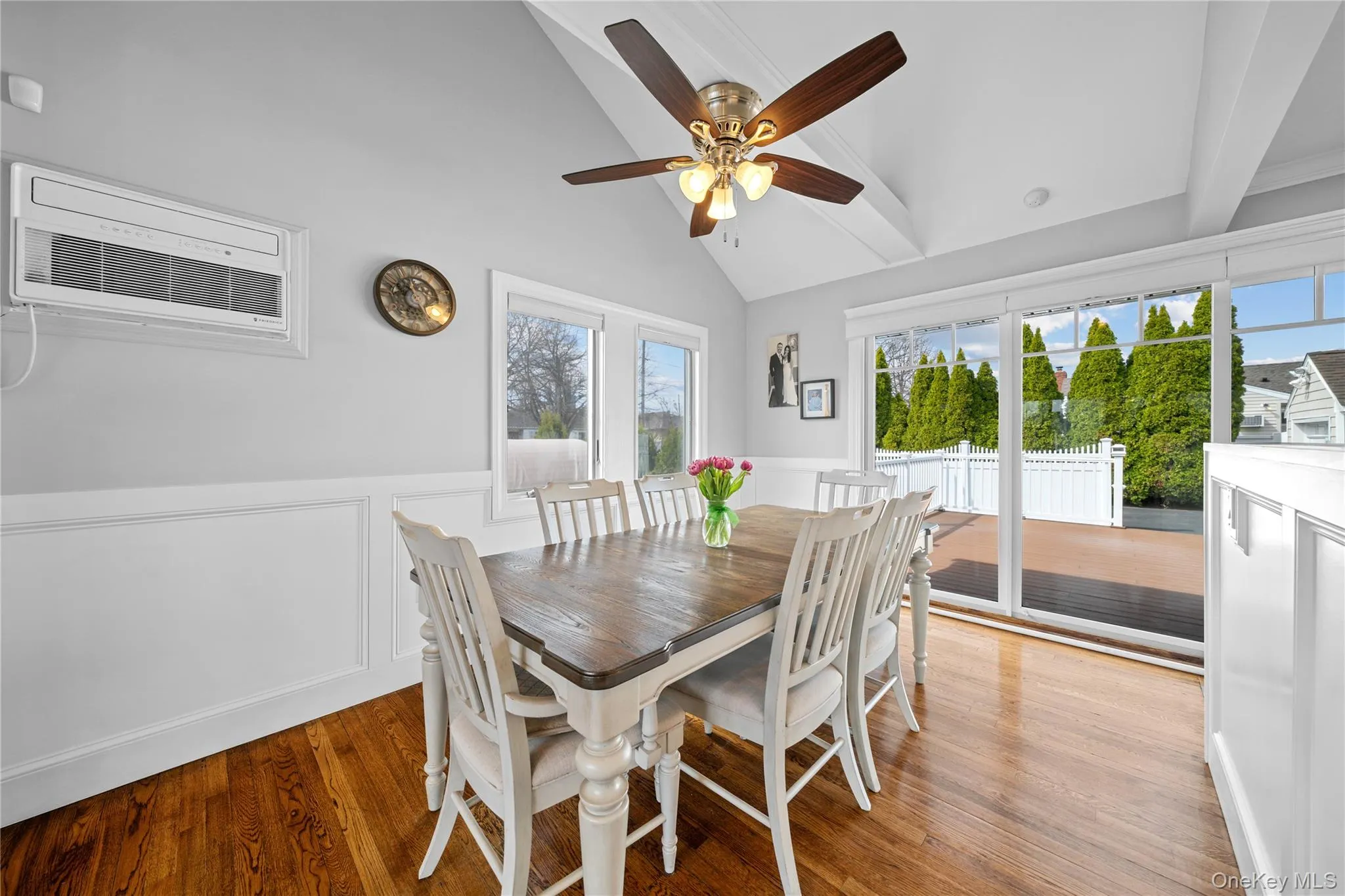 Dining space featuring wainscoting, a ceiling fan, light wood-style floors, lofted ceiling, and a decorative wall Dining space featuring wainscoting, a ceiling fan, light wood-style floors, lofted ceiling, and a decorative wall
