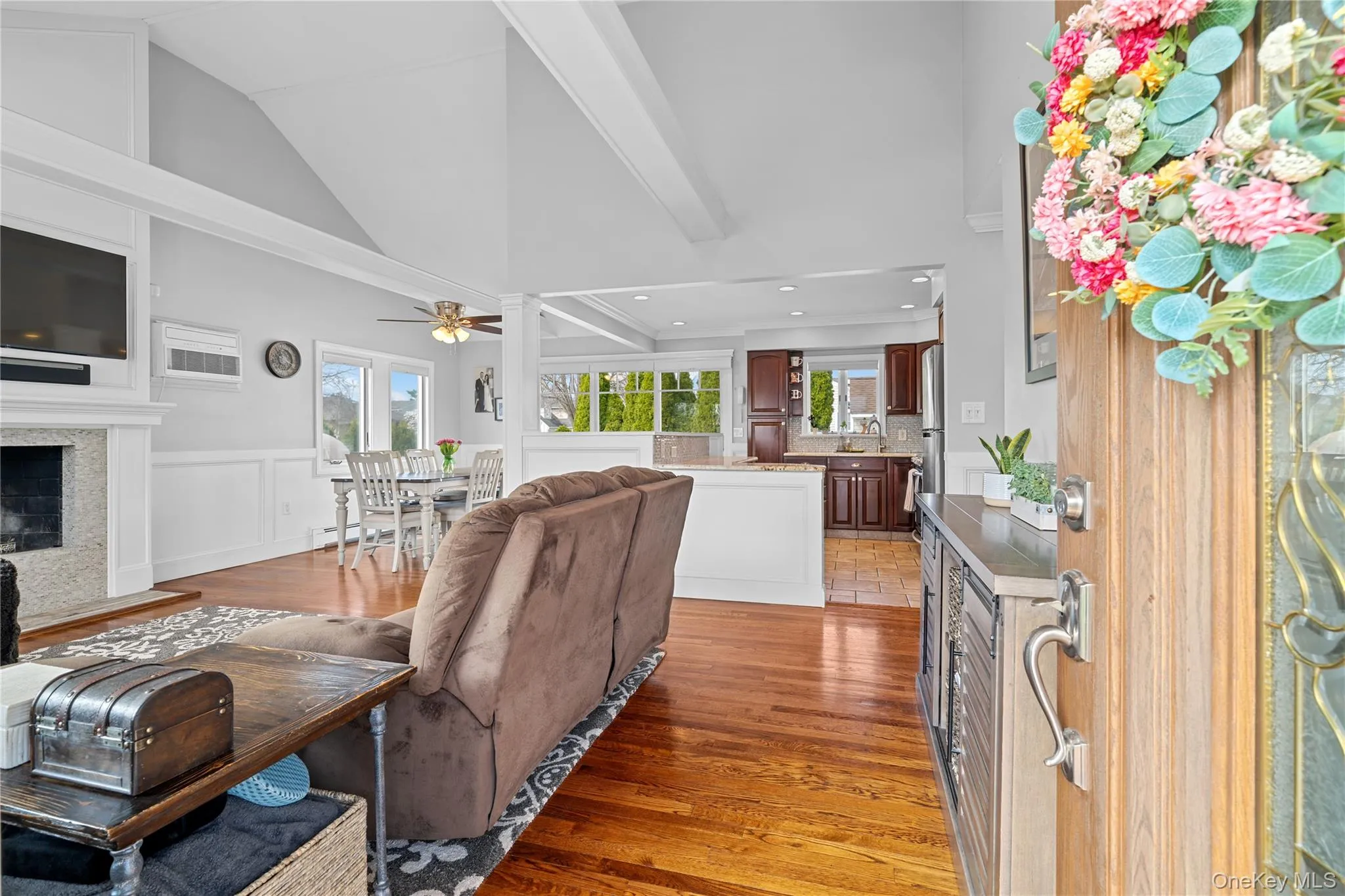 Living room with light wood-style flooring, a fireplace, lofted ceiling, wainscoting, and a decorative wall Living room with light wood-style flooring, a fireplace, lofted ceiling, wainscoting, and a decorative wall