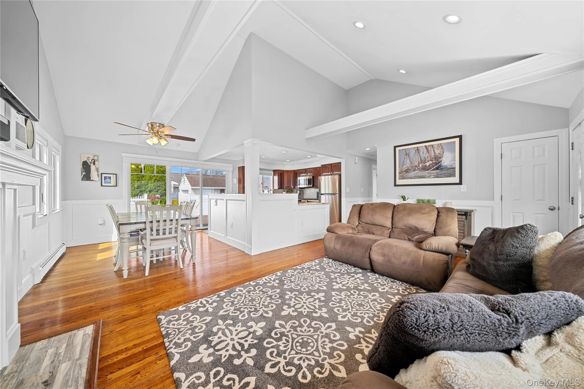 Living room featuring a decorative wall, wainscoting, vaulted ceiling, light wood-style flooring, and baseboard heating Living room featuring a decorative wall, wainscoting, vaulted ceiling, light wood-style flooring, and baseboard heating