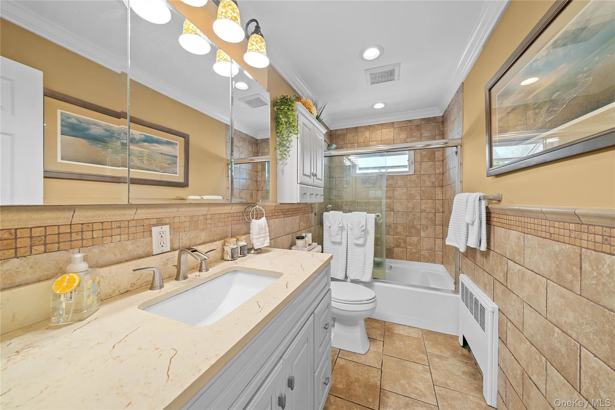 Full bathroom featuring tile walls, vanity, bath / shower combo with glass door, radiator, and ornamental molding Full bathroom featuring tile walls, vanity, bath / shower combo with glass door, radiator, and ornamental molding