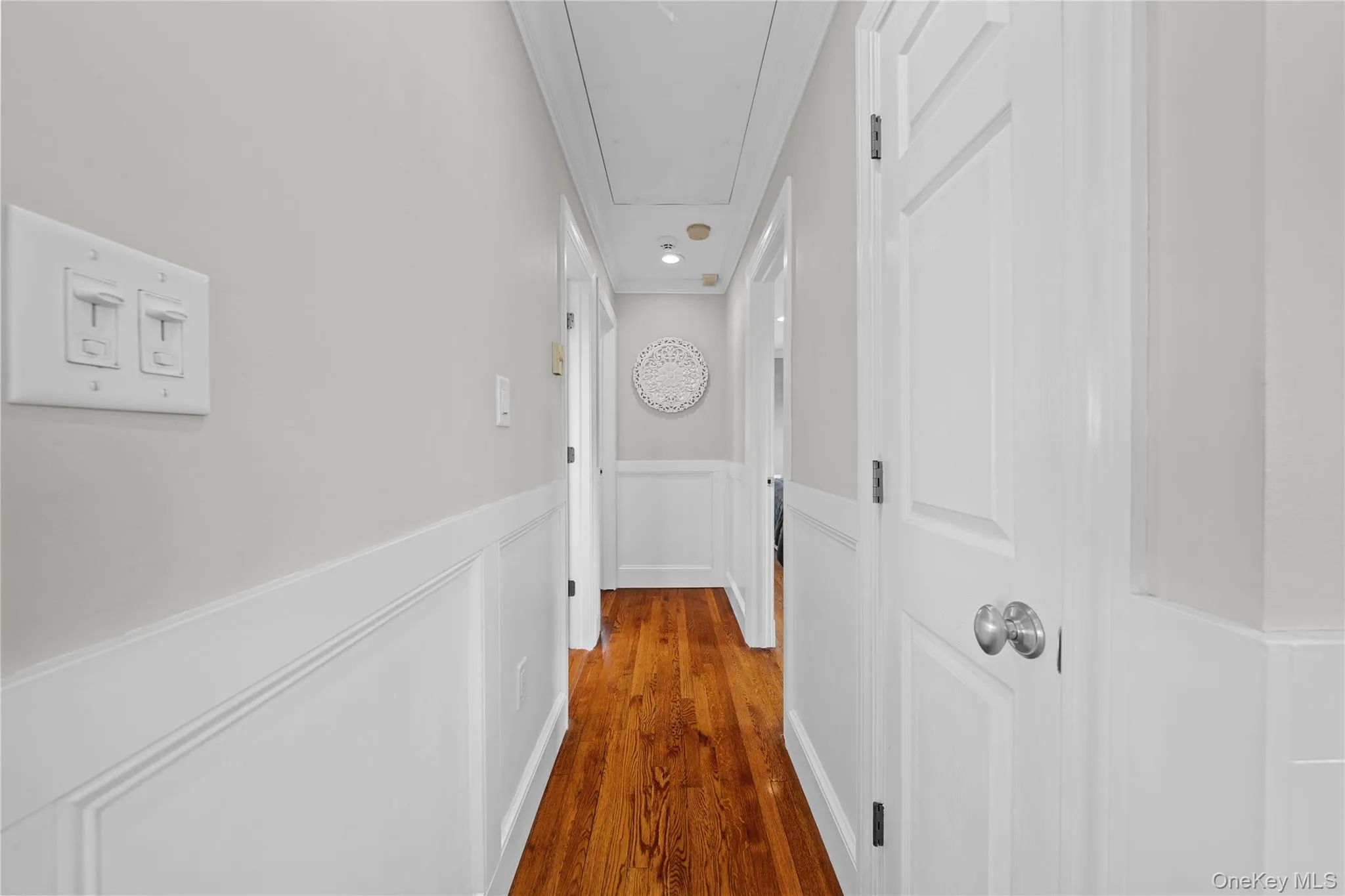 Hall featuring wainscoting, wood finished floors, and a decorative wall Hall featuring wainscoting, wood finished floors, and a decorative wall