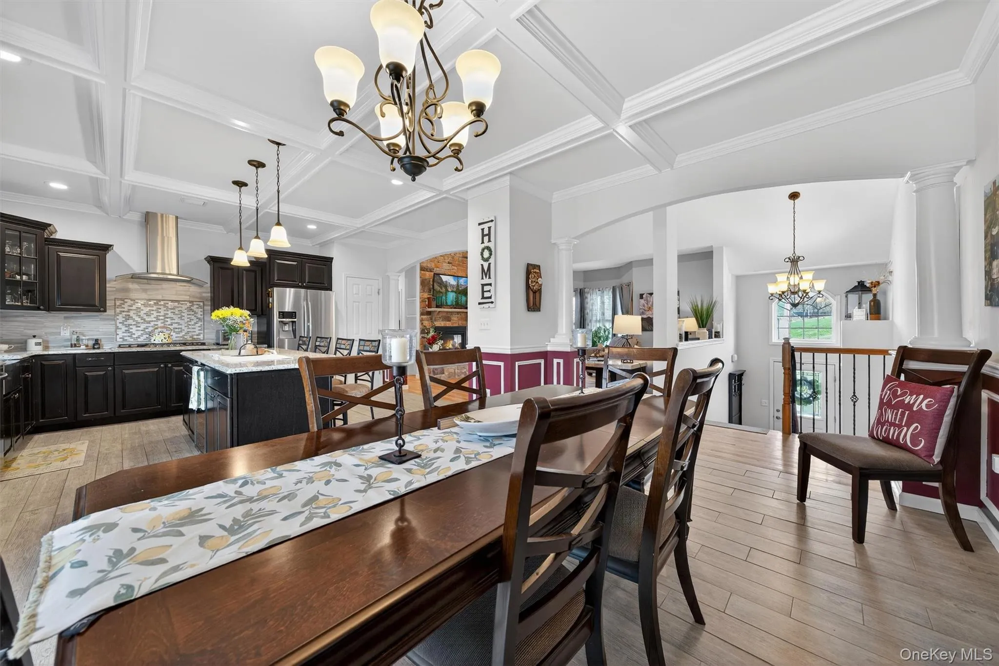 Dining space featuring suspended lighting, arched walkways, light wood-style floors, coffered ceiling, and ornate columns Dining space featuring suspended lighting, arched walkways, light wood-style floors, coffered ceiling, and ornate columns