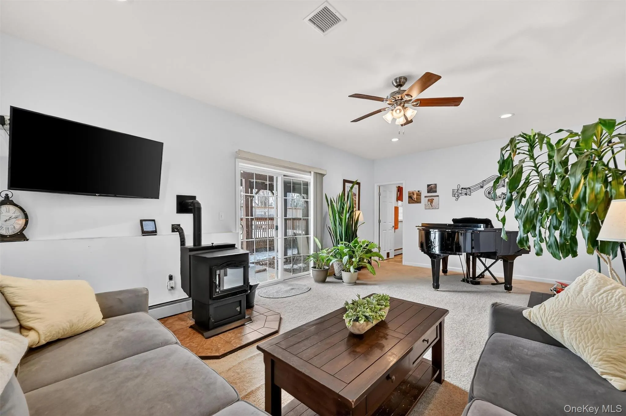 Living room featuring a wood stove, recessed lighting, carpet flooring, a baseboard radiator, and a ceiling fan Living room featuring a wood stove, recessed lighting, carpet flooring, a baseboard radiator, and a ceiling fan