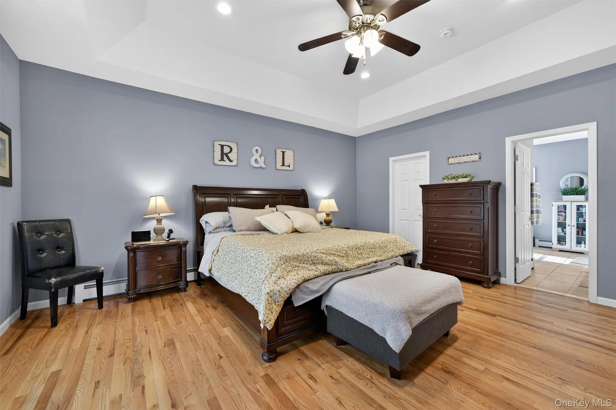 Bedroom featuring a baseboard radiator, light wood finished floors, a raised ceiling, ceiling fan, and recessed lighting Bedroom featuring a baseboard radiator, light wood finished floors, a raised ceiling, ceiling fan, and recessed lighting