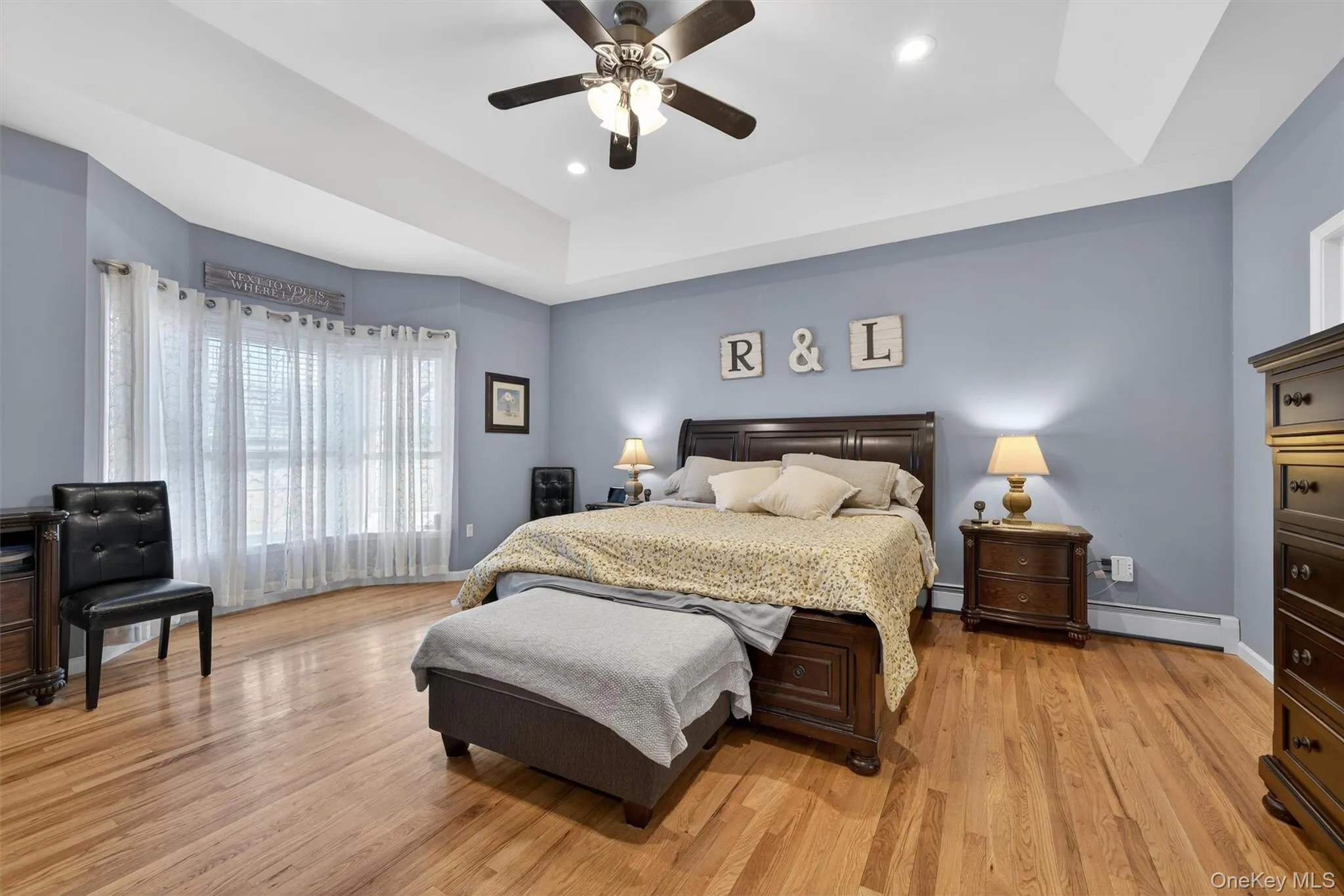 Bedroom with a raised ceiling, light wood-style flooring, baseboard heating, ceiling fan, and recessed lighting Bedroom with a raised ceiling, light wood-style flooring, baseboard heating, ceiling fan, and recessed lighting