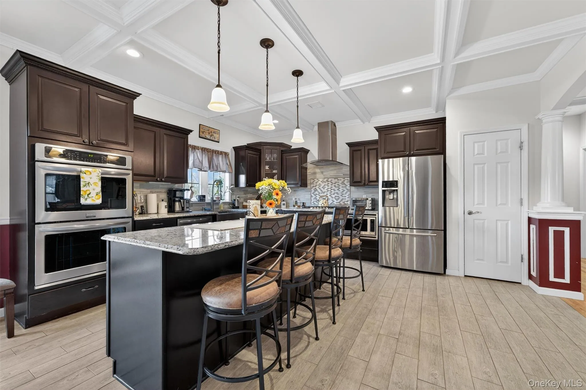 Kitchen featuring dark wood finish cabinets, stainless steel appliances, ornate columns, a center island, and light wood-type flooring Kitchen featuring dark wood finish cabinets, stainless steel appliances, ornate columns, a center island, and light wood-type flooring