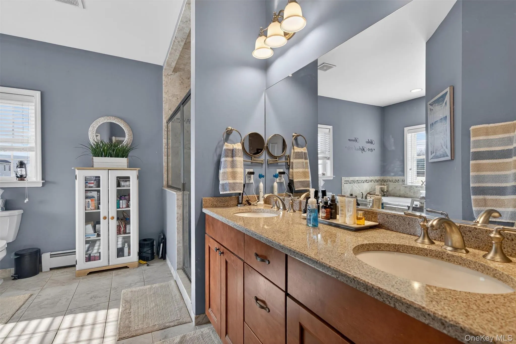 Bathroom featuring double vanity, baseboard heating, a shower stall, and light tile patterned floors Bathroom featuring double vanity, baseboard heating, a shower stall, and light tile patterned floors
