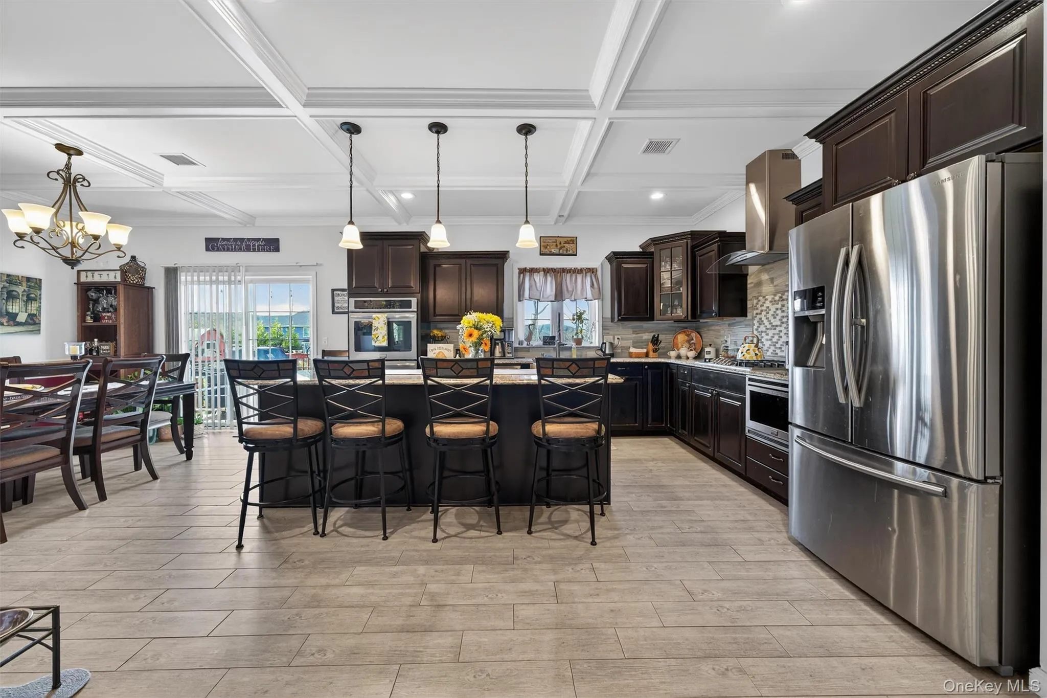 Kitchen featuring stainless steel appliances, dark wood finish cabinetry, a kitchen island, a breakfast bar, and coffered ceiling Kitchen featuring stainless steel appliances, dark wood finish cabinetry, a kitchen island, a breakfast bar, and coffered ceiling