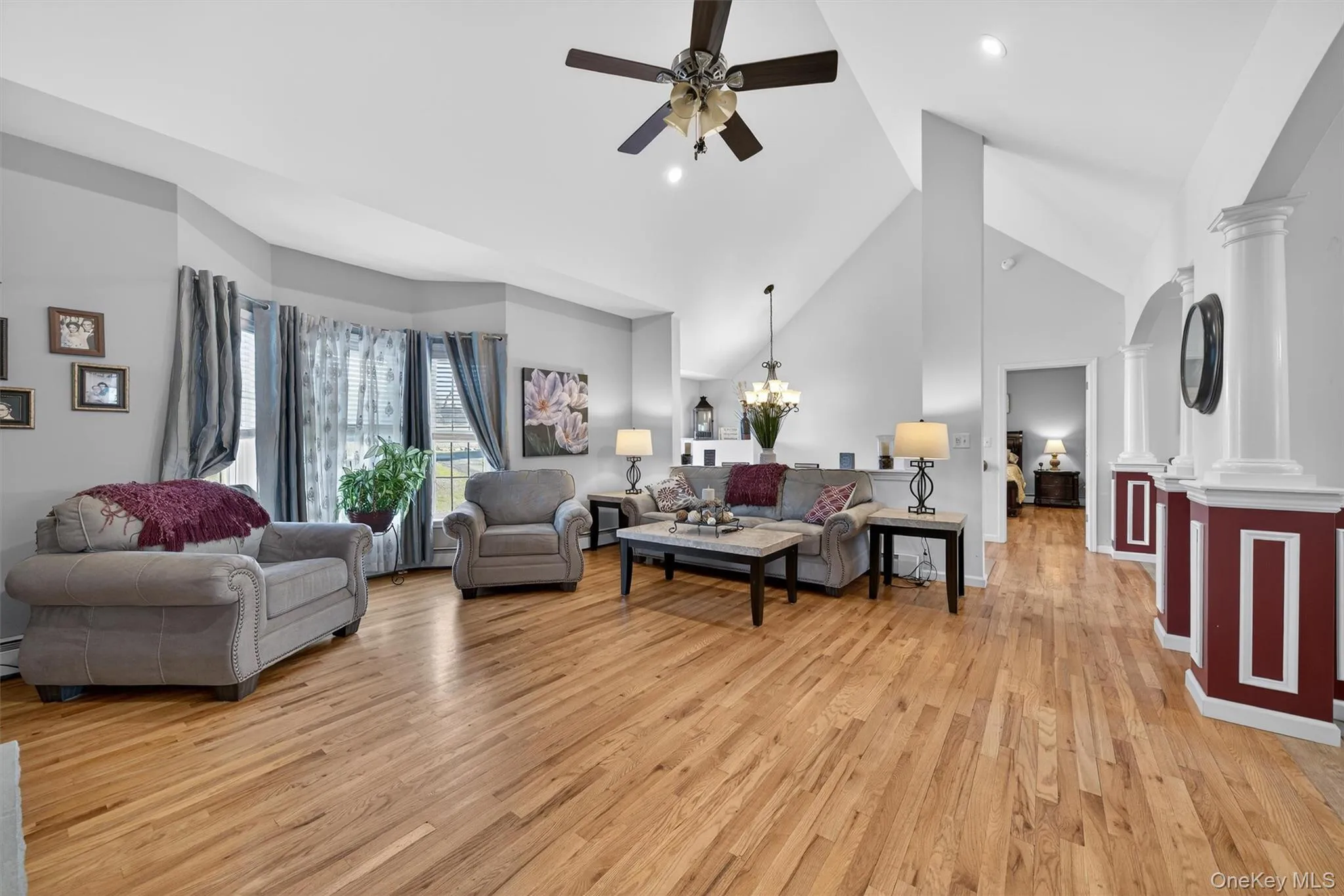 Living area featuring a ceiling fan, light wood finished floors, vaulted ceiling, ornate columns, and suspended lighting Living area featuring a ceiling fan, light wood finished floors, vaulted ceiling, ornate columns, and suspended lighting