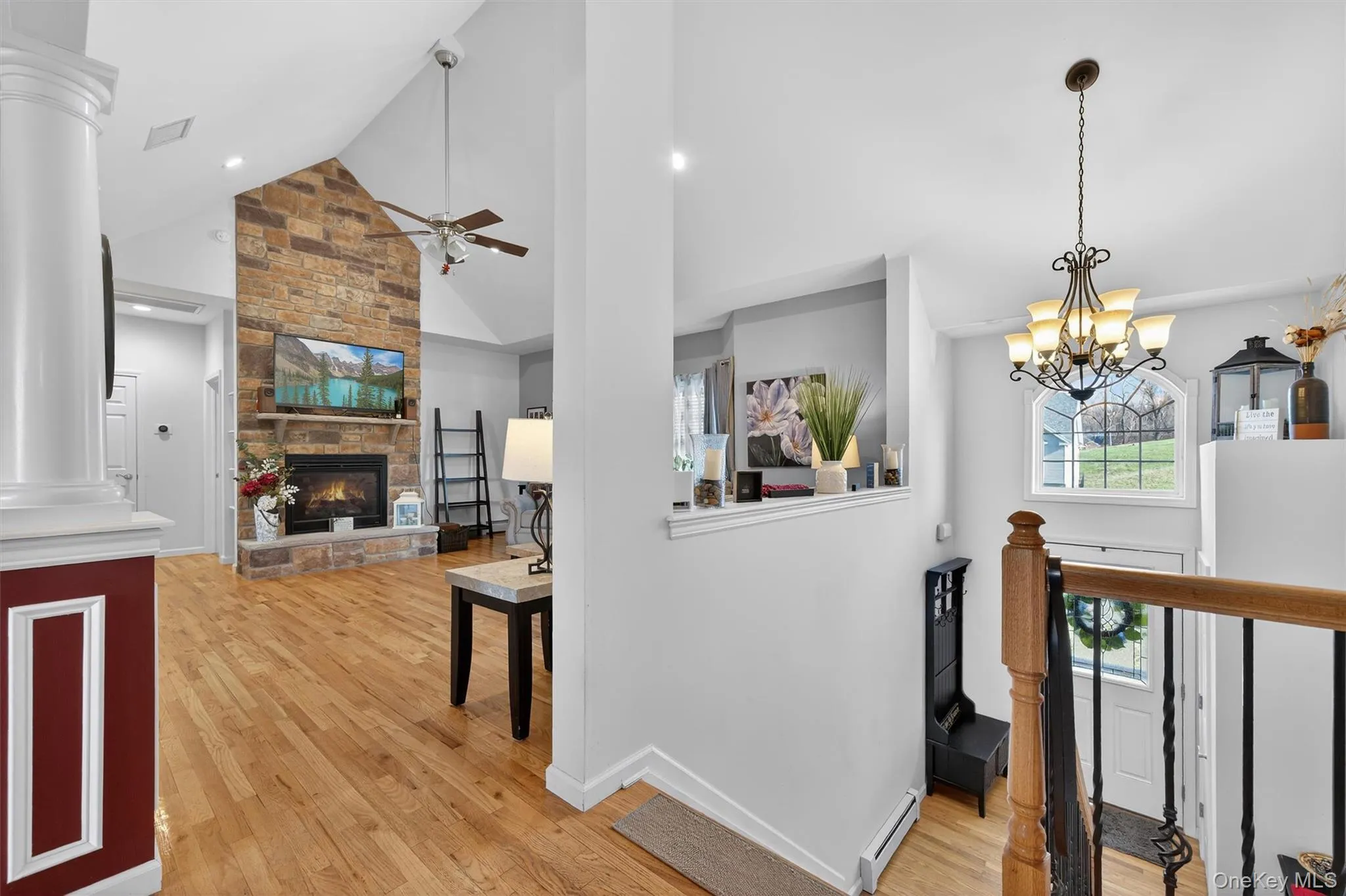 Hall with light wood-type flooring, lofted ceiling, ornate columns, a baseboard radiator, and a chandelier Hall with light wood-type flooring, lofted ceiling, ornate columns, a baseboard radiator, and a chandelier