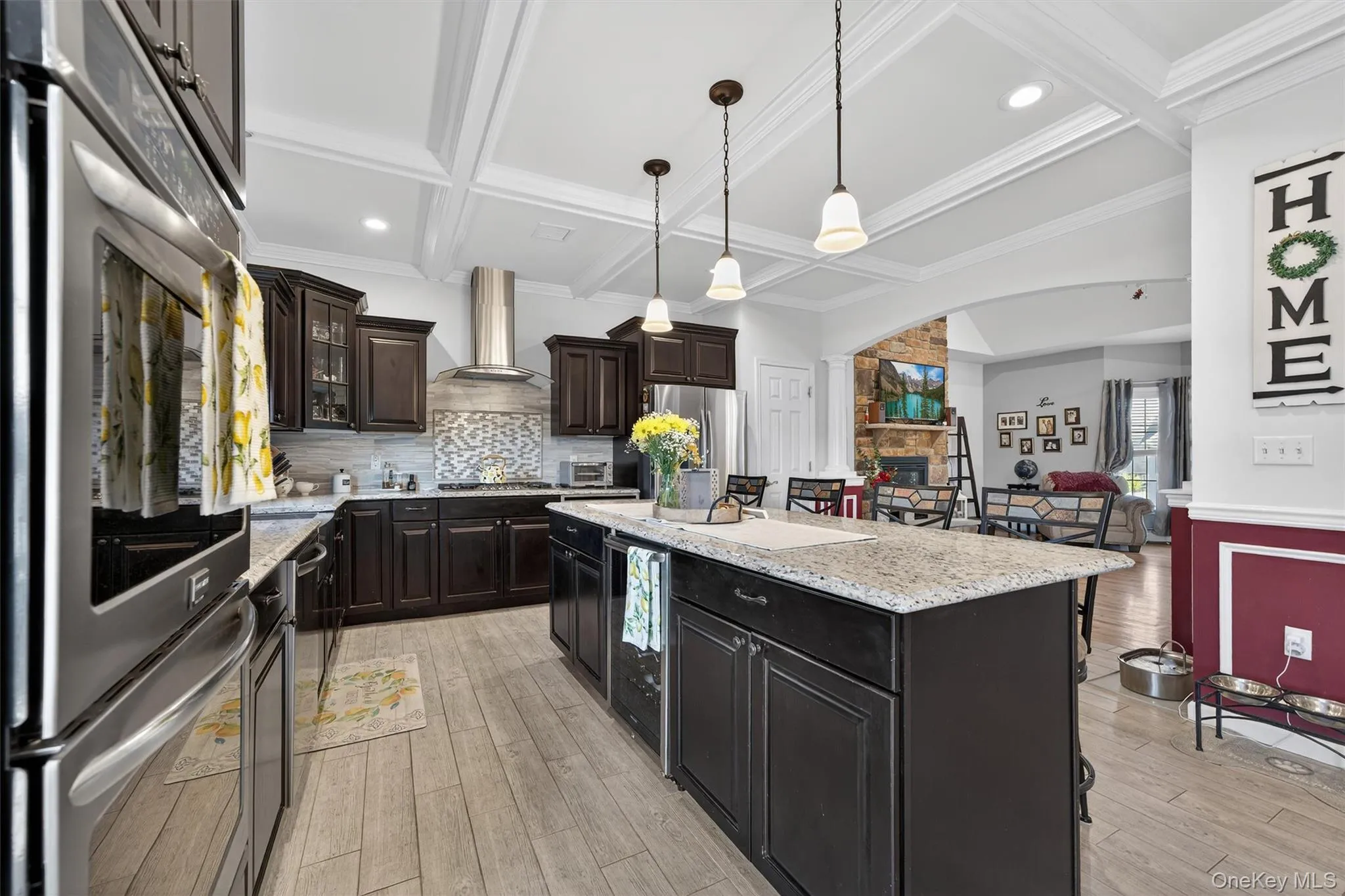 Kitchen featuring stainless steel appliances, a center island, coffered ceiling, light stone counters, and light wood finished floors Kitchen featuring stainless steel appliances, a center island, coffered ceiling, light stone counters, and light wood finished floors