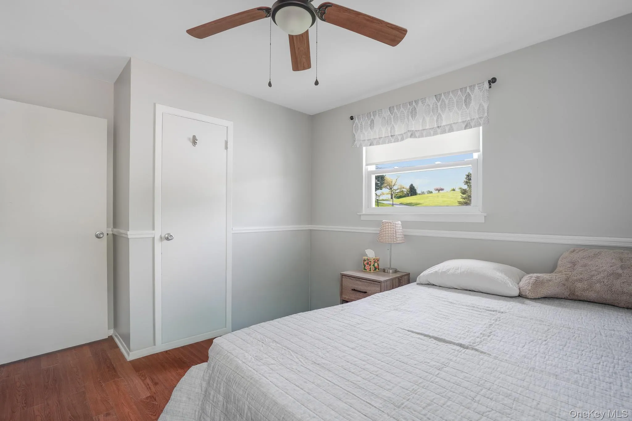Light-filled room featuring wood-finish flooring, a ceiling fan with wood-look blades, and white trim molding throughout Light-filled room featuring wood-finish flooring, a ceiling fan with wood-look blades, and white trim molding throughout