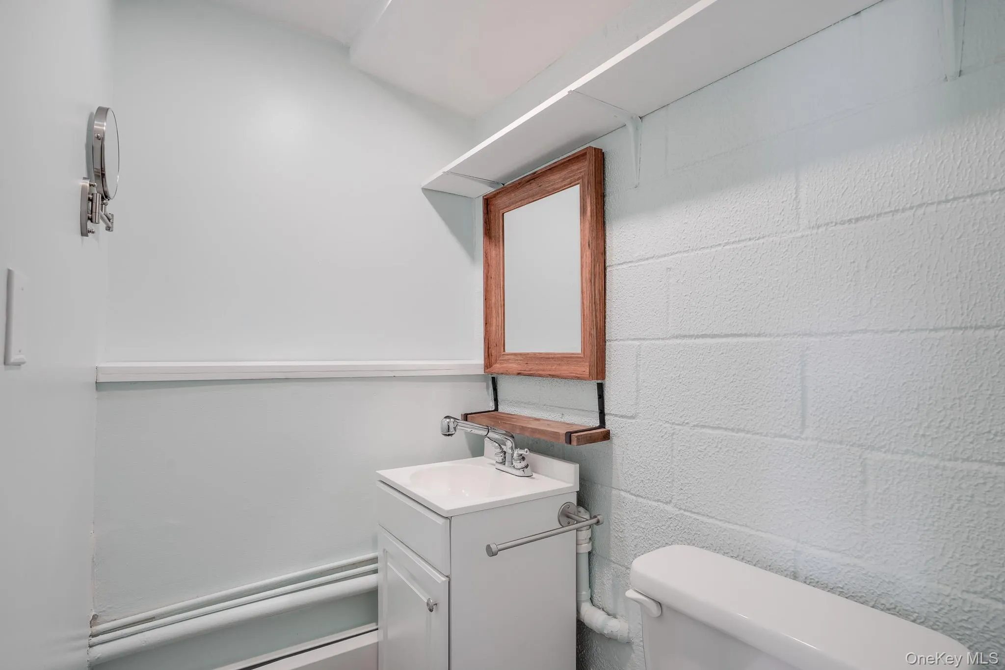 Bathroom featuring a white vanity with integrated sink, a framed mirror with an accent shelf, and block wall texture Bathroom featuring a white vanity with integrated sink, a framed mirror with an accent shelf, and block wall texture