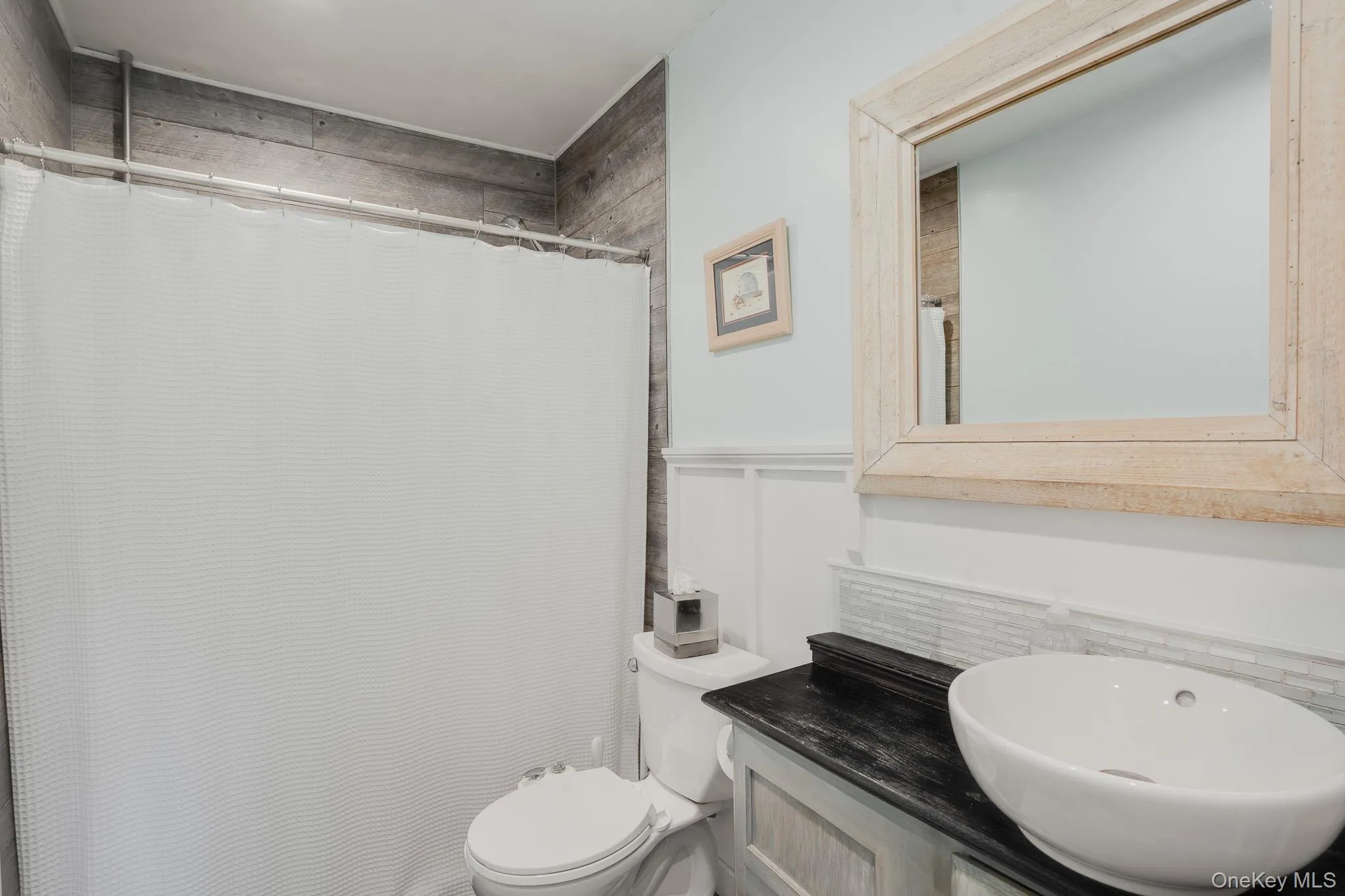 Bathroom featuring a vessel sink, dark countertop, and wood-finish accent wall paneling Bathroom featuring a vessel sink, dark countertop, and wood-finish accent wall paneling