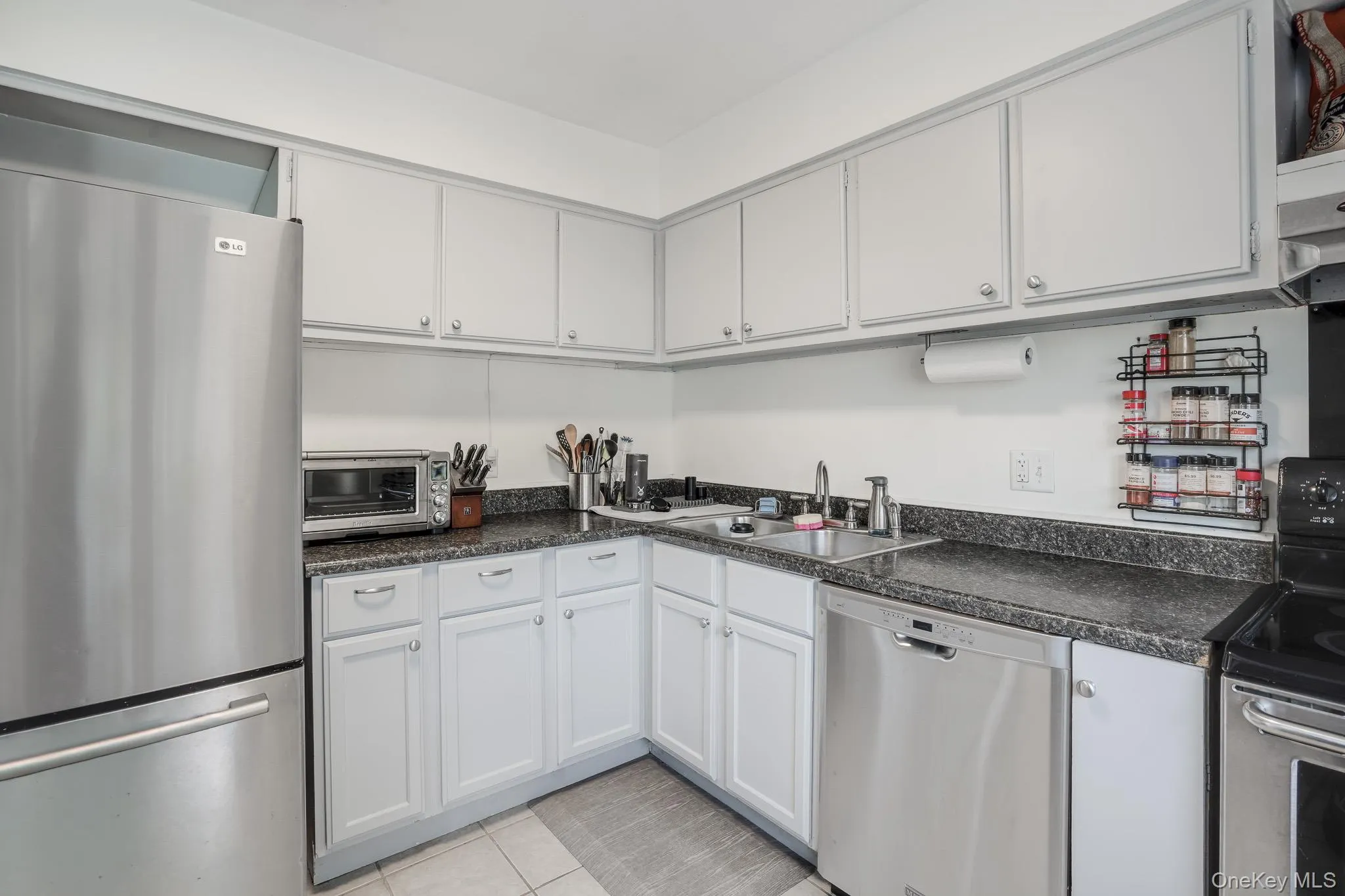 Kitchen featuring white cabinetry, dark speckled countertops, stainless steel refrigerator, stainless steel dishwasher, and tile flooring Kitchen featuring white cabinetry, dark speckled countertops, stainless steel refrigerator, stainless steel dishwasher, and tile flooring