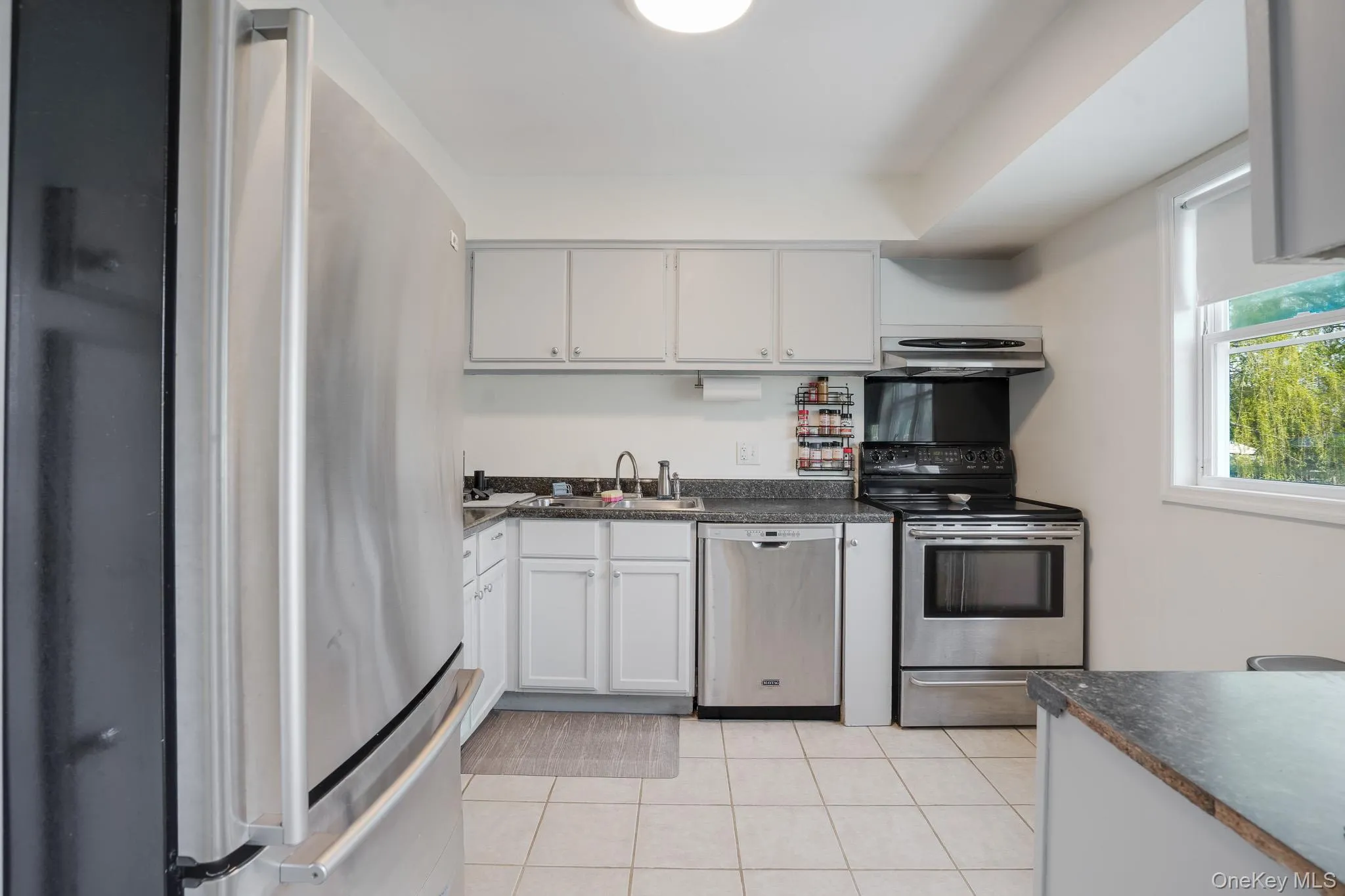 Kitchen featuring stainless steel appliances, white cabinetry, dark countertops, a window, and tile flooring Kitchen featuring stainless steel appliances, white cabinetry, dark countertops, a window, and tile flooring