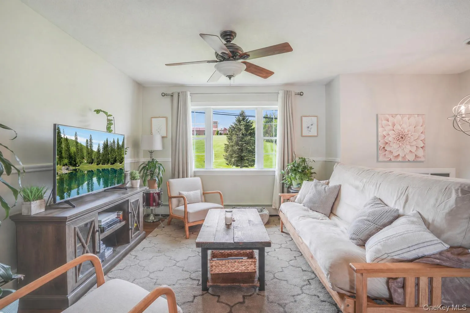 Bright living area featuring a large window, a ceiling fan with integrated lighting, wood-finish flooring, and a decorative area rug Bright living area featuring a large window, a ceiling fan with integrated lighting, wood-finish flooring, and a decorative area rug